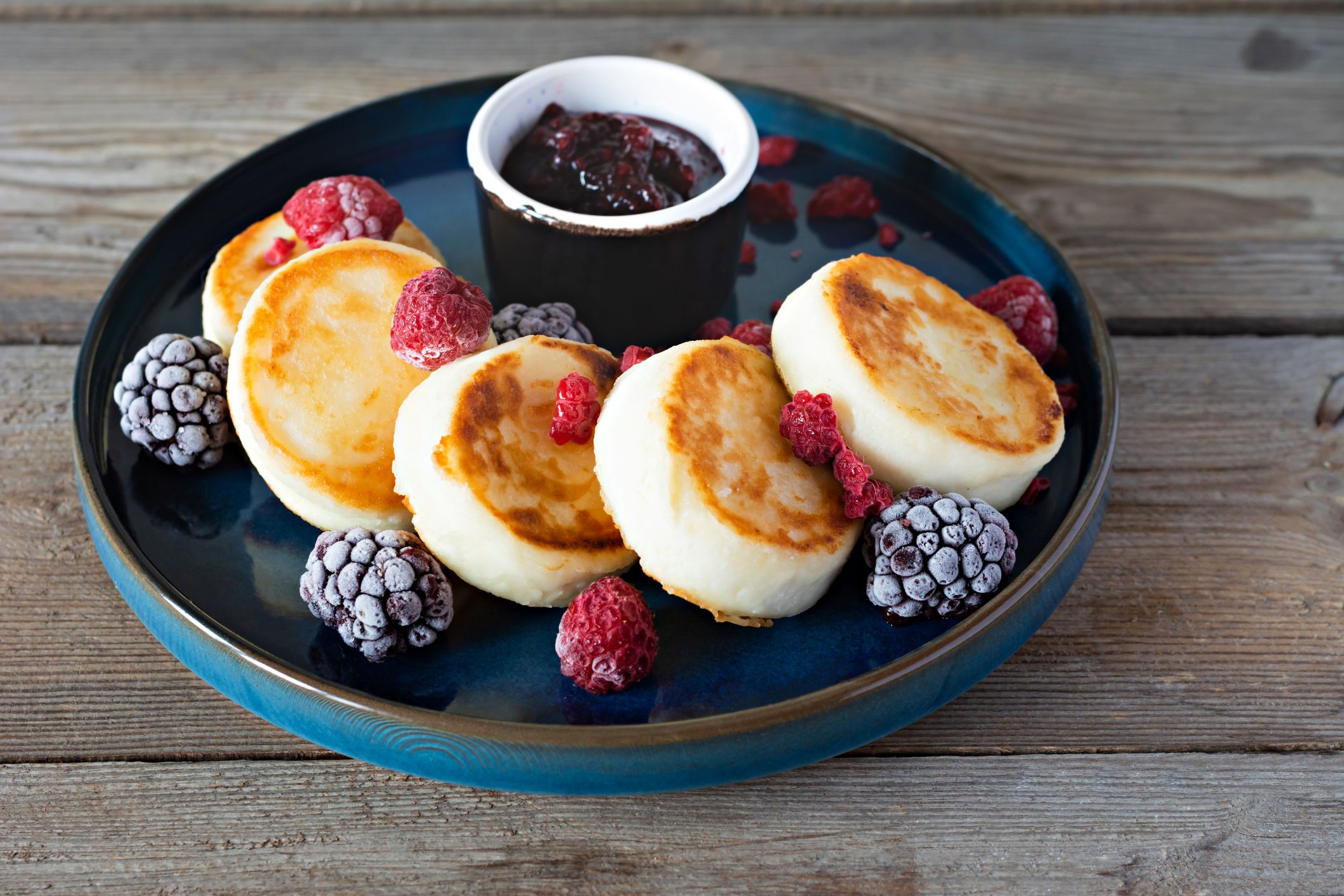 Fresh cottage cheese or ricotta pancakes (syrniki,fritters) on a blue plate with fresh berries and jam. Delicious healthy cottage cheese breakfast. Ukrainian, Russian cuisine sweet food
