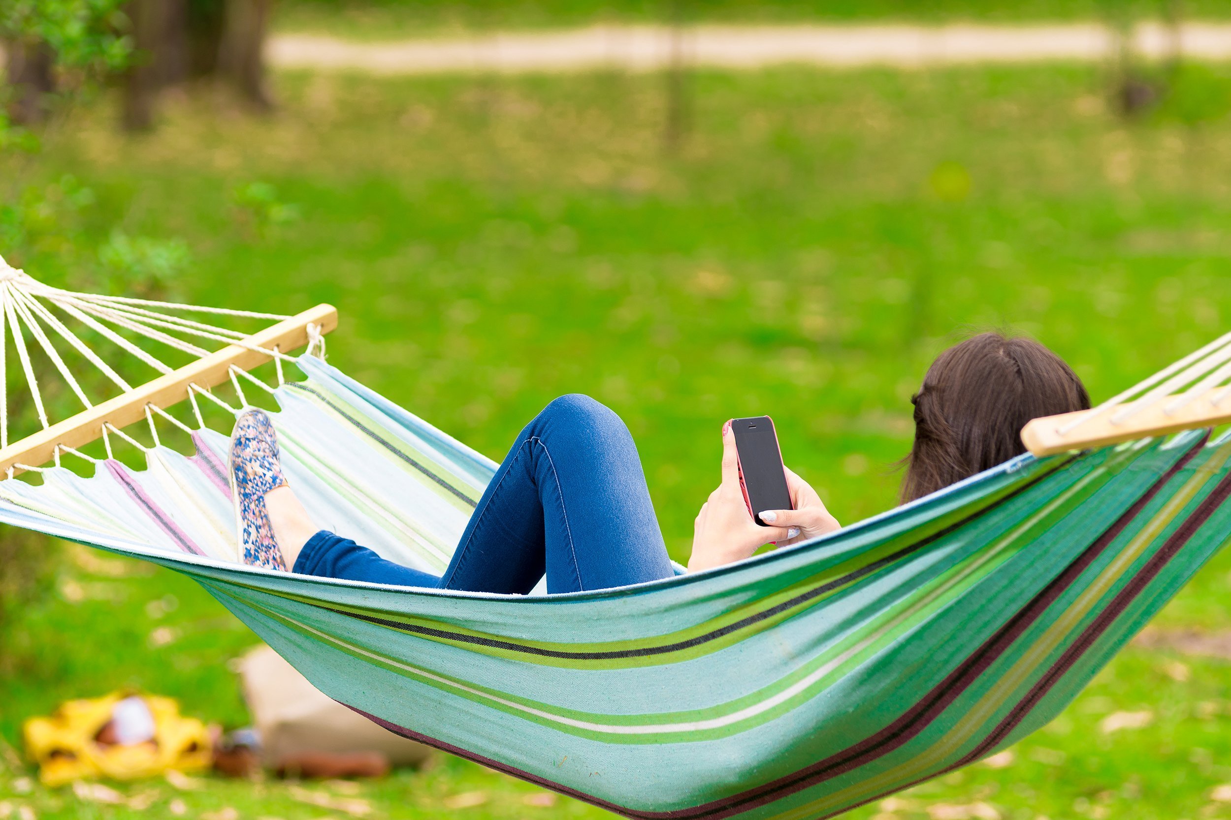 rear view of young girl lying on a hammock looking at her cell phone