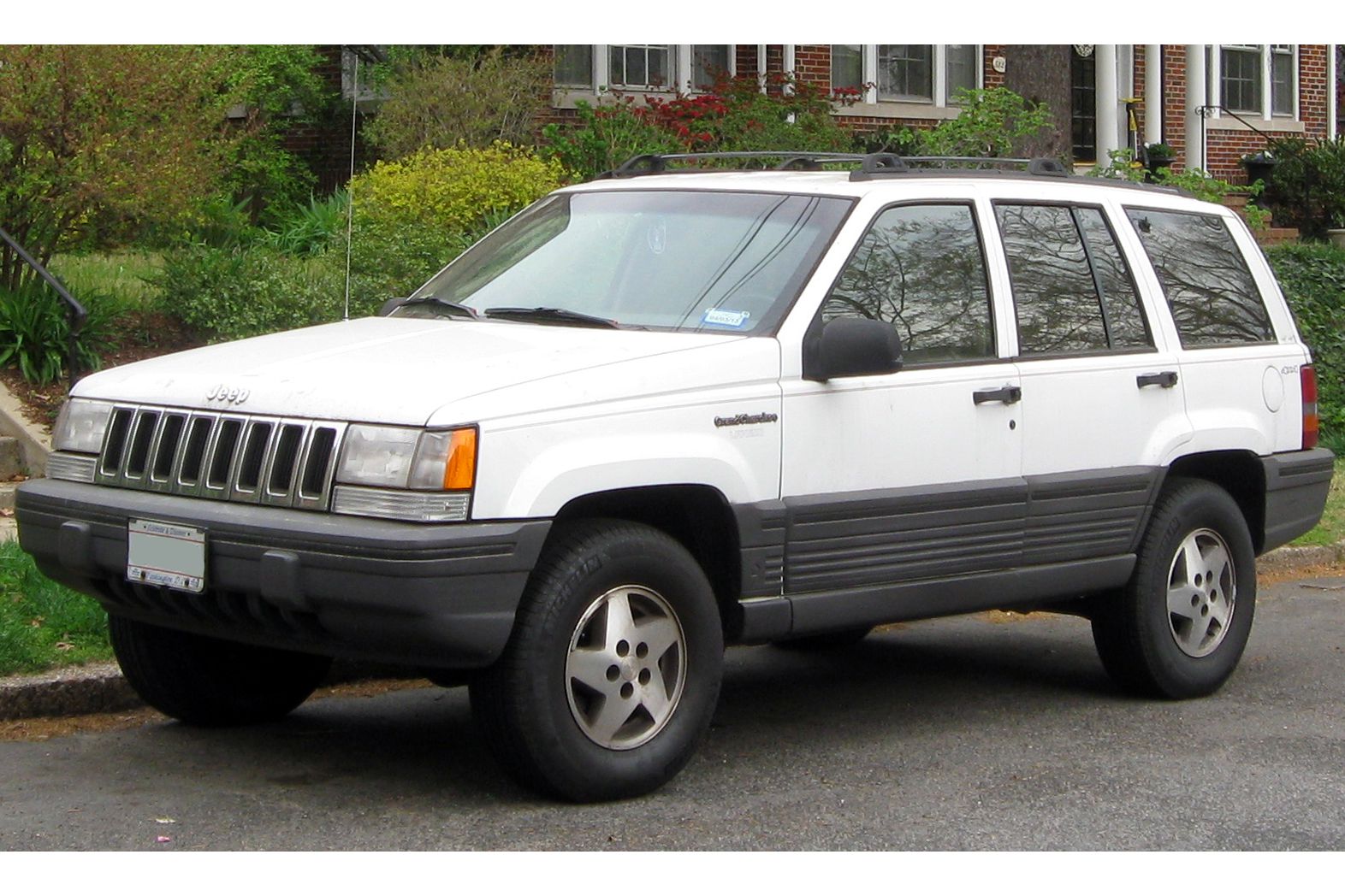 White 1992 Jeep Grand Cherokee parked on street in front of brick row houses on a summer day.