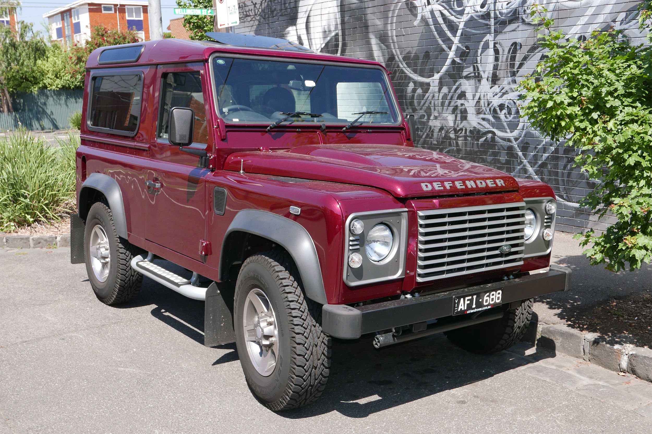 Red 2015 Land Rover Defender parked on street in front of graffiti