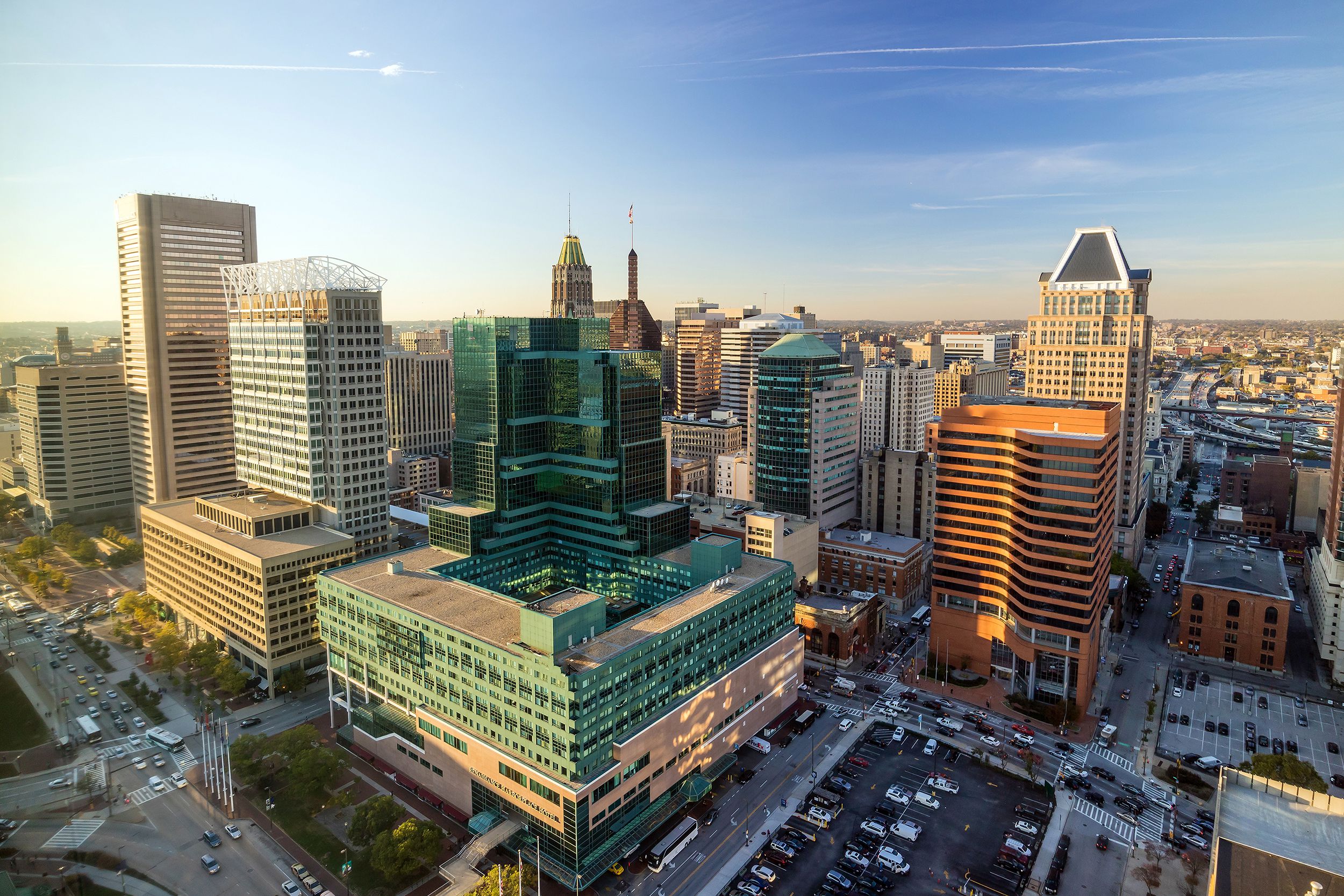 Aerial of downtown Baltimore, Maryland, buildings and cars on streets and parked in parking lots, sunlight coming through left side