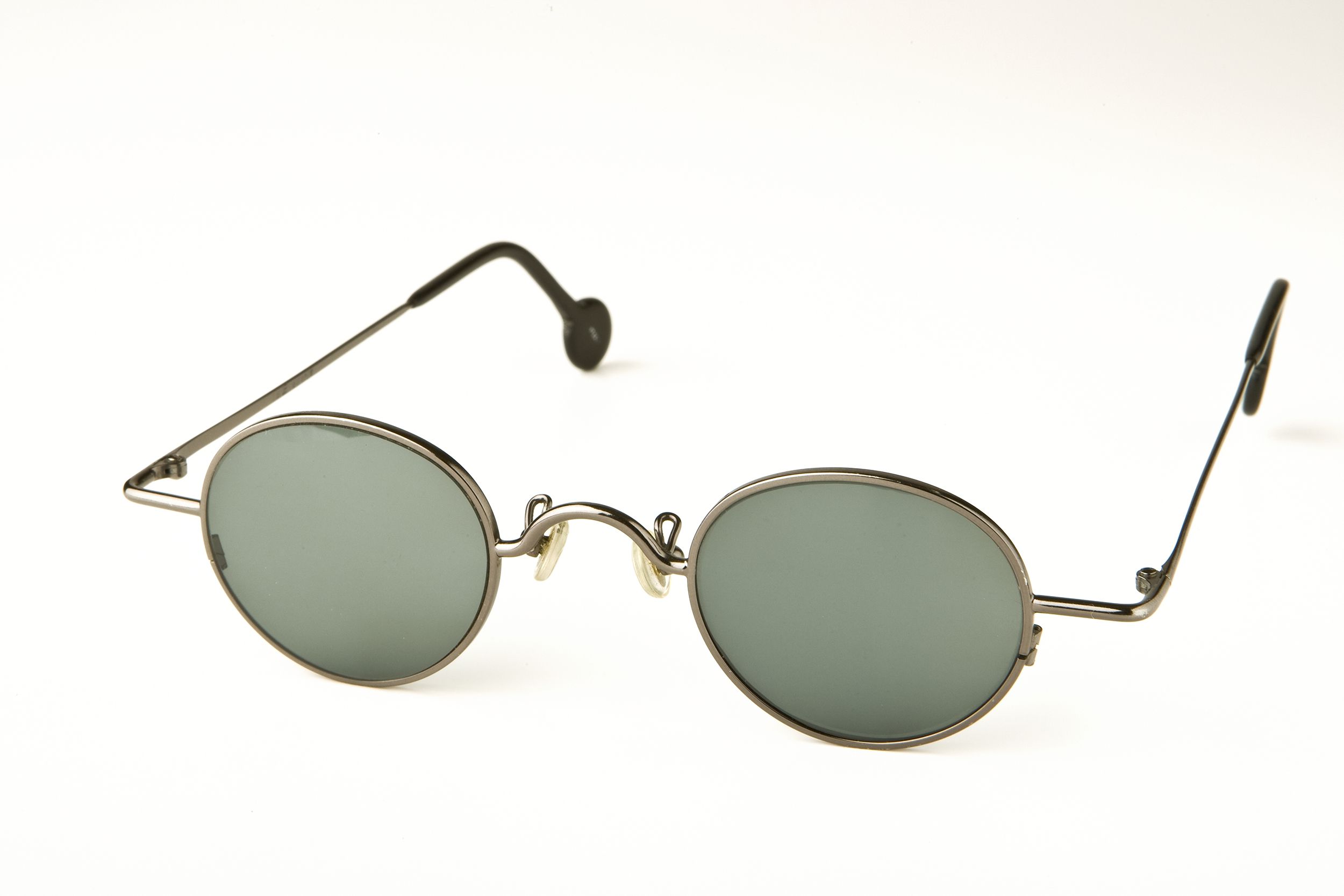 Chrome rimmed John Lennon styled sunglasses with grey lenses and black ear grips on a white background