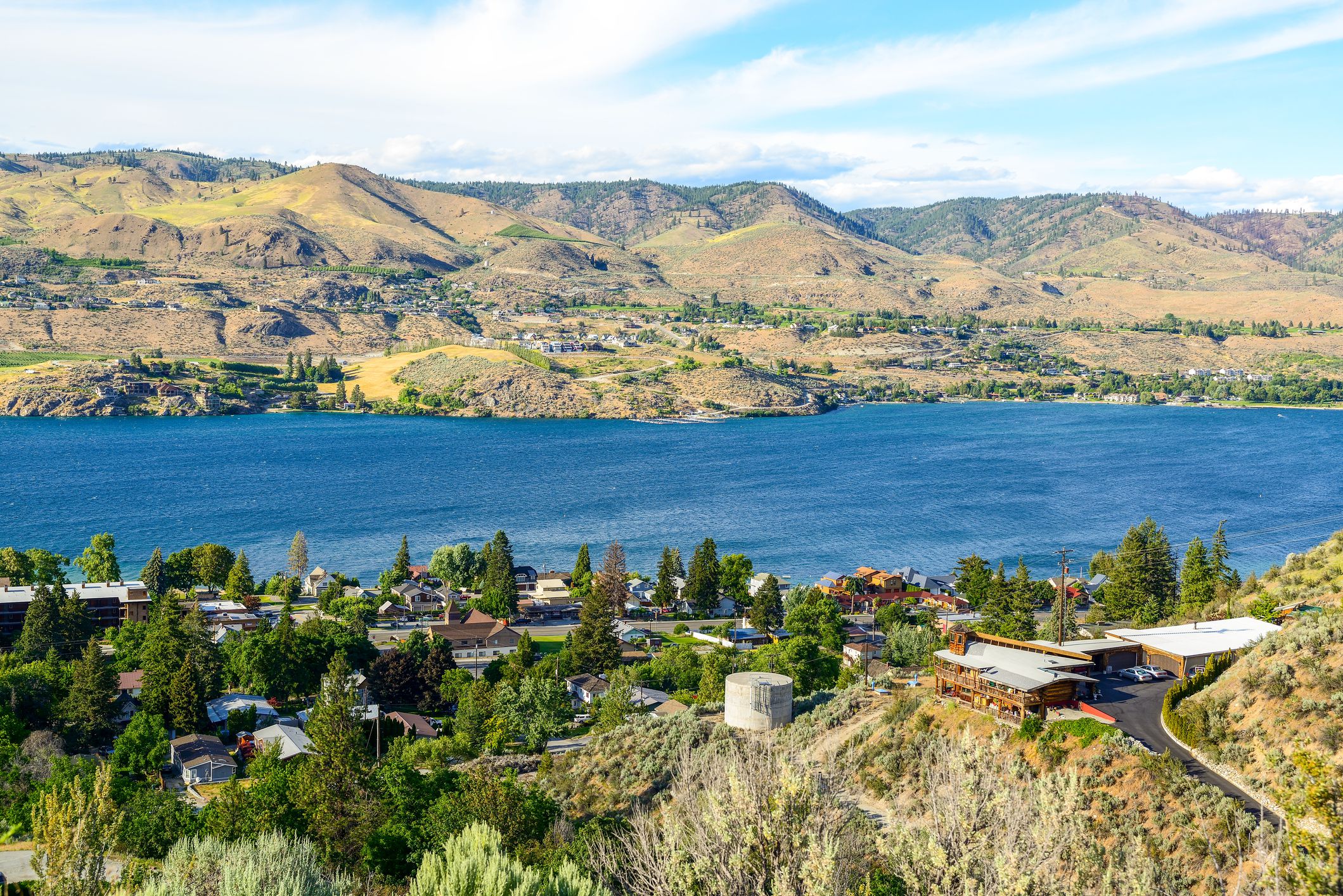 Lake Chelan, Washington, homes in the foreground and on the other side of it in the background, on a sunny day