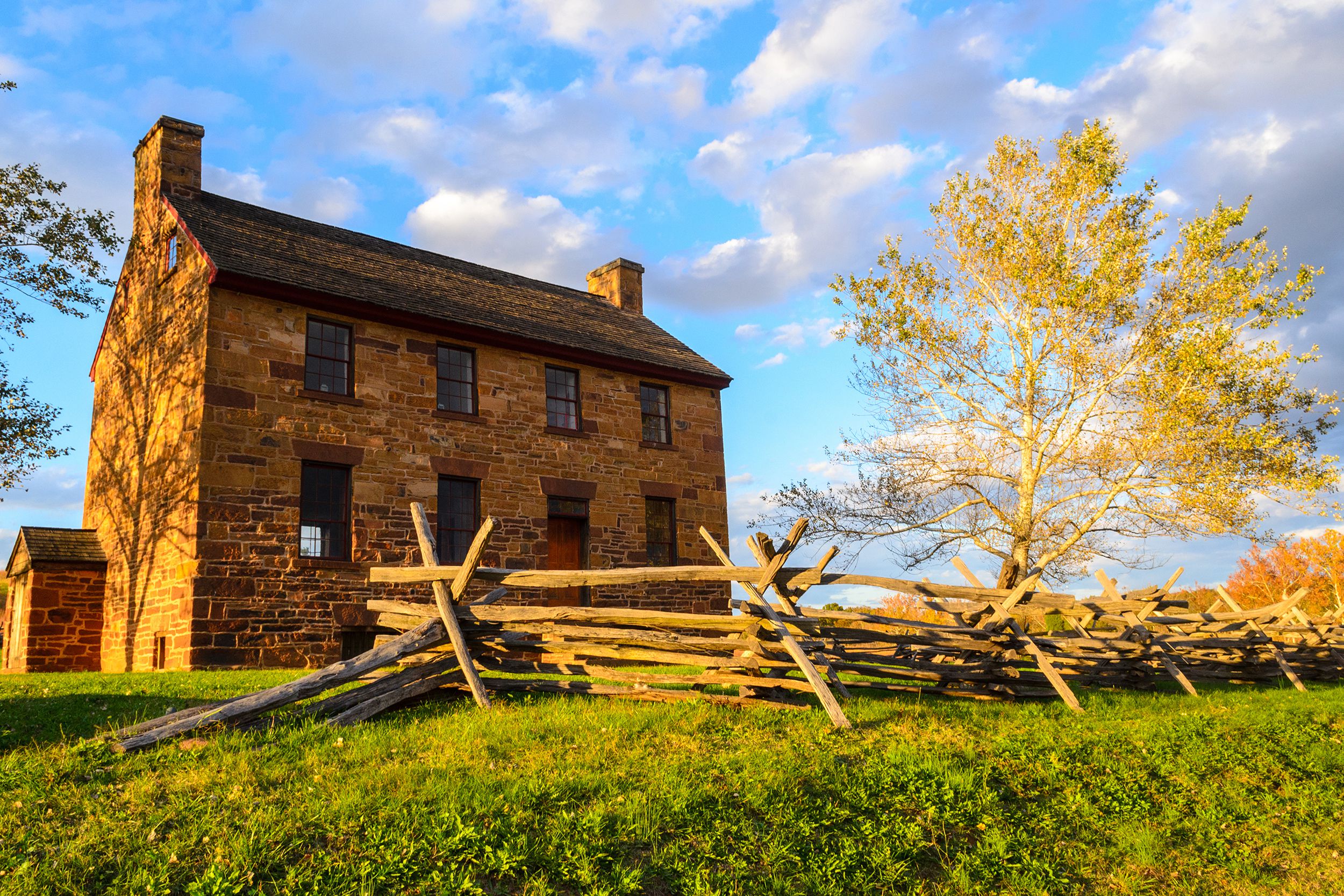 Historic stone house at Manassas National Battlefield Park, Manassas, Virginia, wooden fence in the foreground, grass and trees, during before sunset