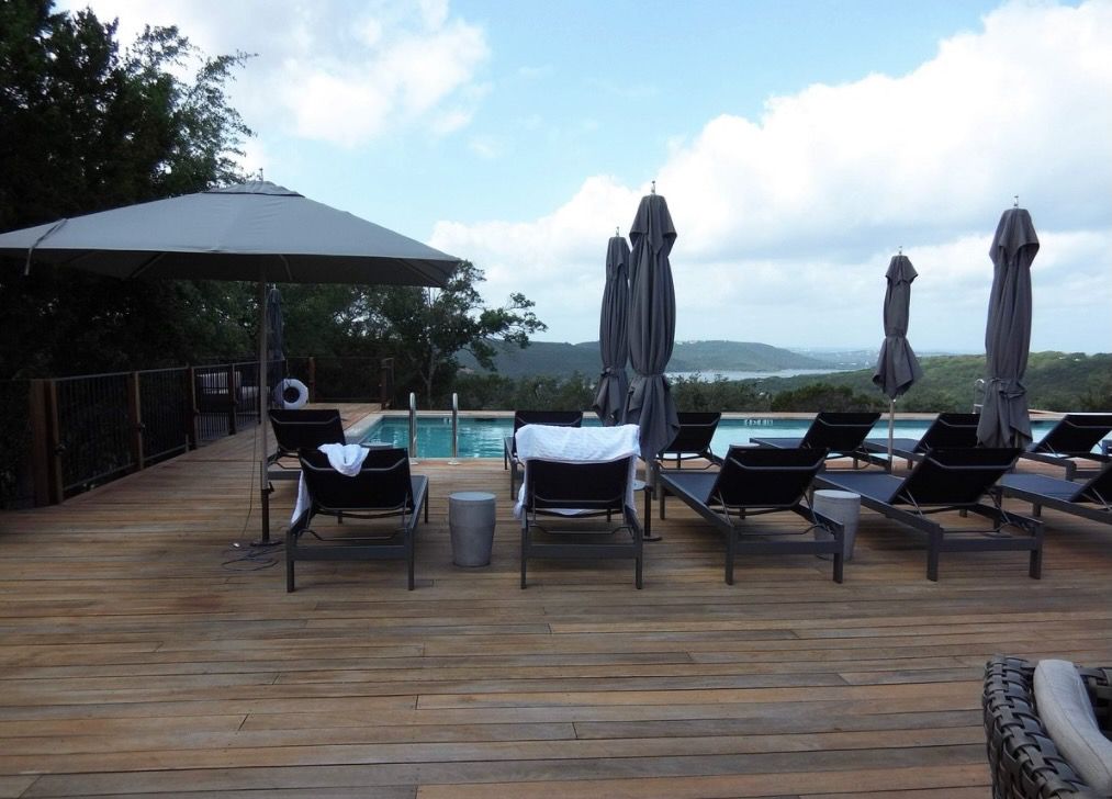 Lounge chairs on a huge deck overlooking a pool and a lake.