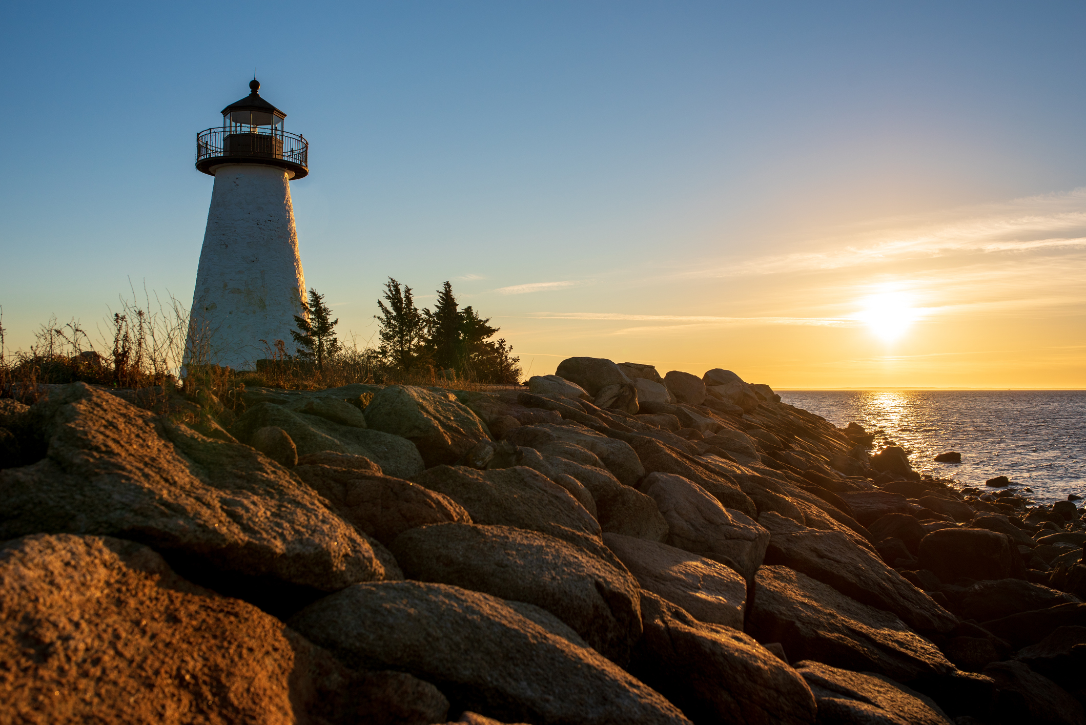 Ned Point Lighthouse in Mattapoisett, Massachusetts during sunrise, rocks in the foreground, sun and ocean in the background
