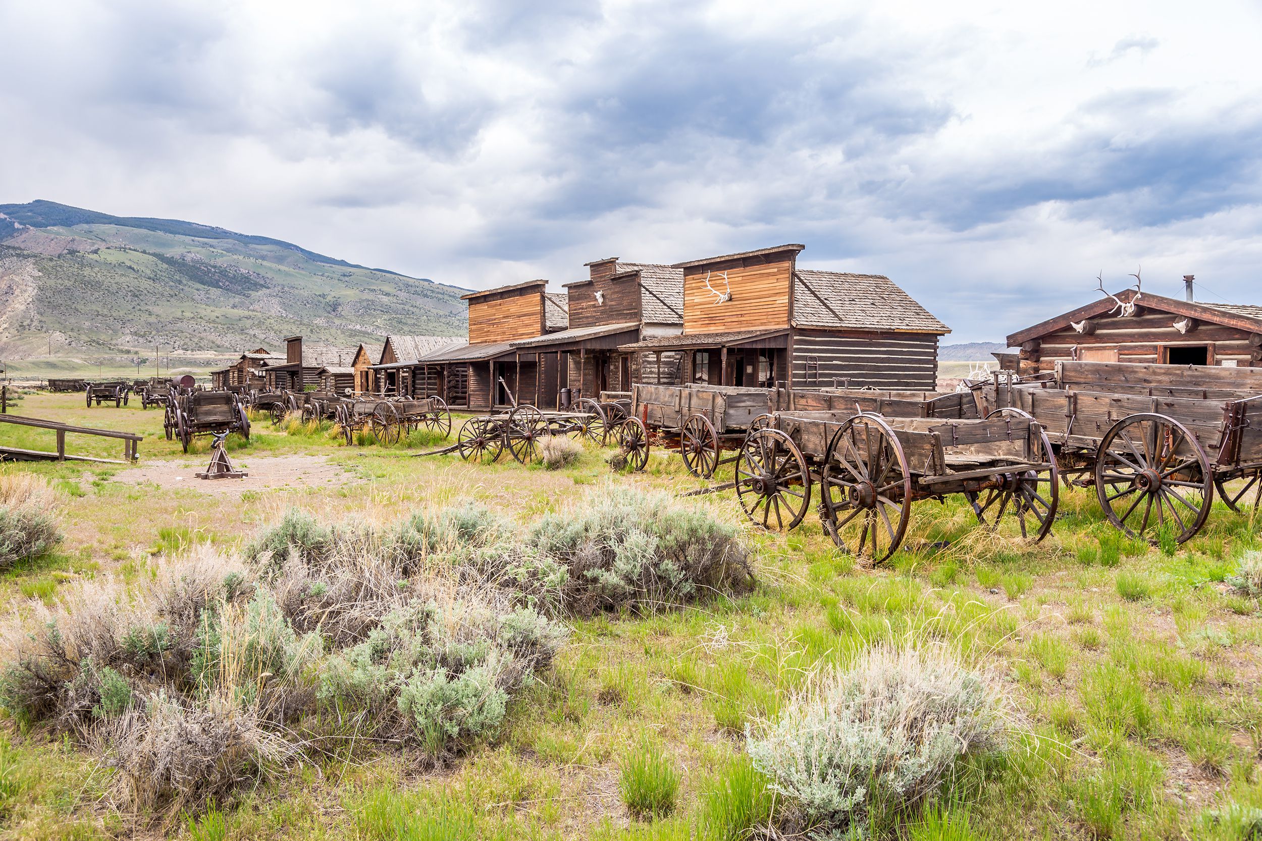 Old Trail Town with historic western buildings, Cody, Wyoming, sagebrush in the foreground with wooden wagons, mountains in the background