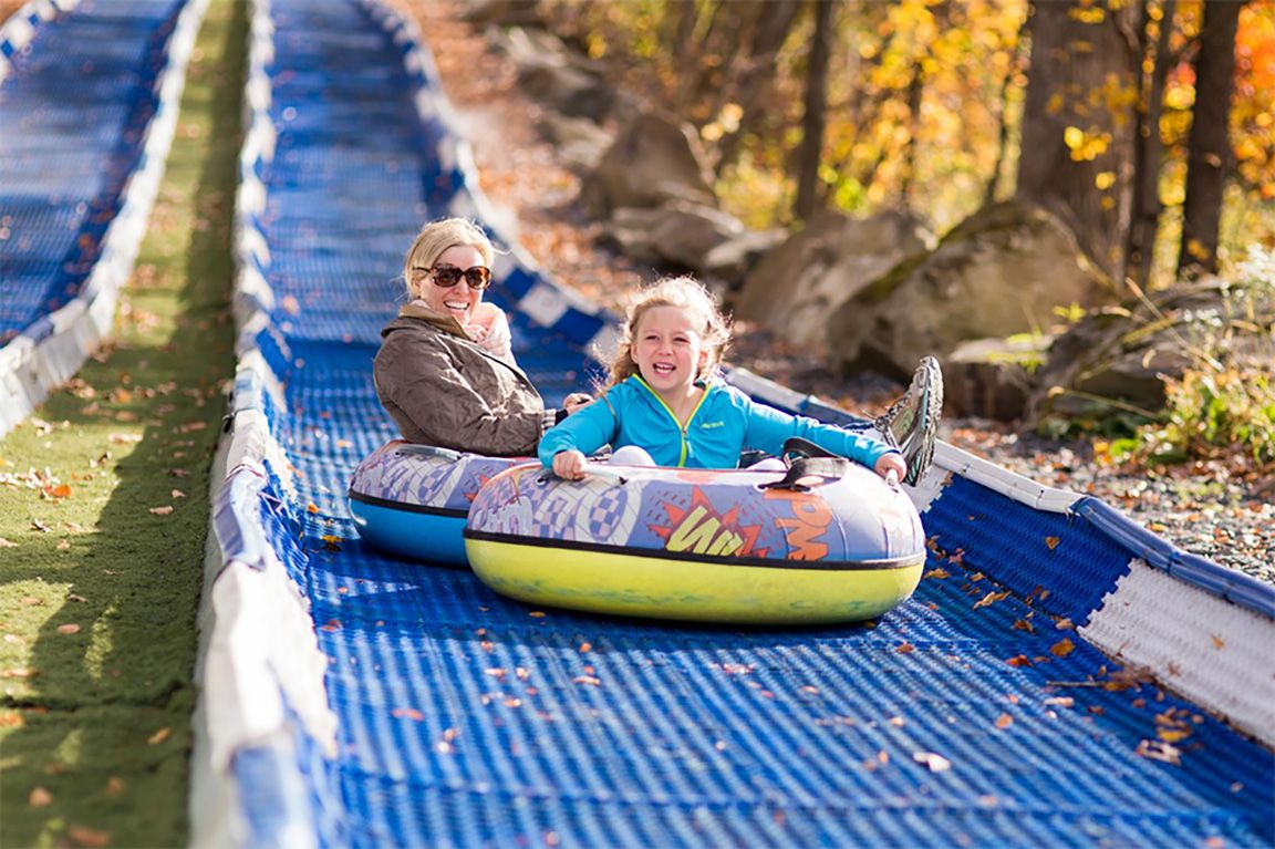 Mom and daughter tubing down a slide on a sunny autumn day.