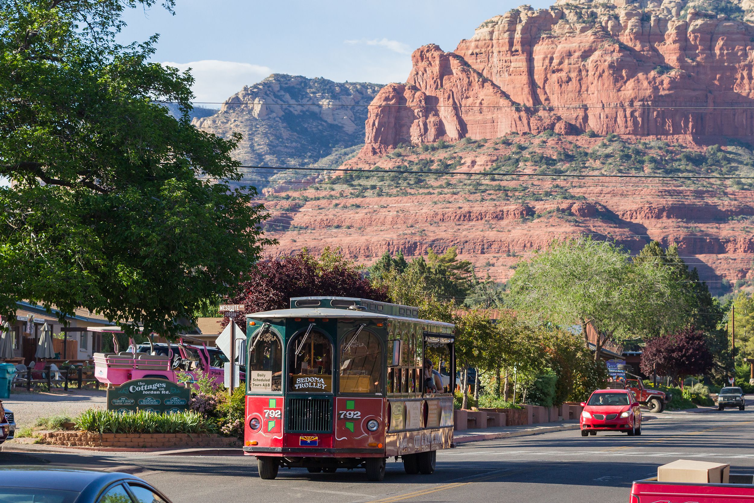 Sedona Trolley on road going through downtown Sedona, Arizona, cars and shops, red mountains in the background