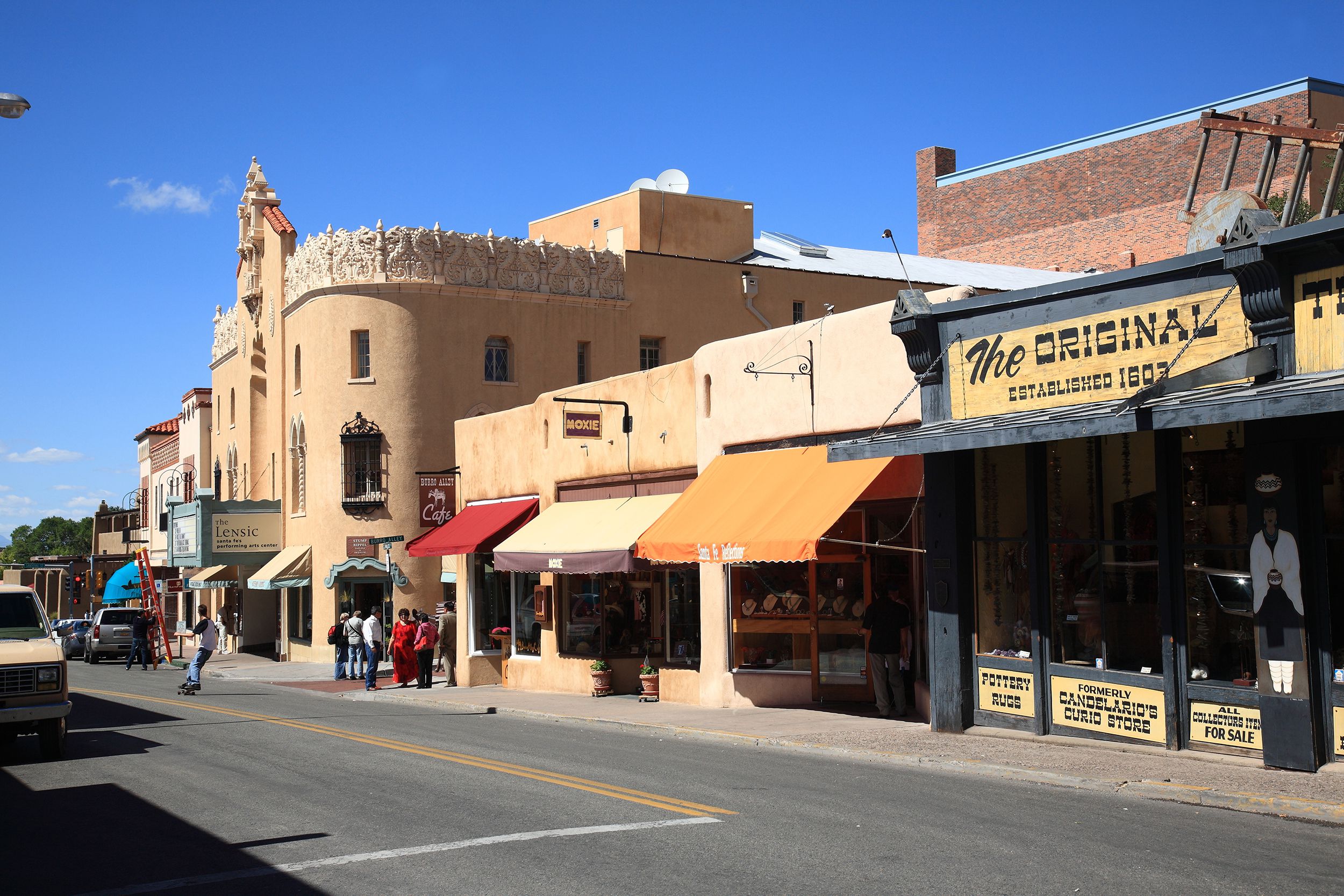Terracotta style buildings along a street in downtown Santa Fe, New Mexico, people out with cars, on a sunny day