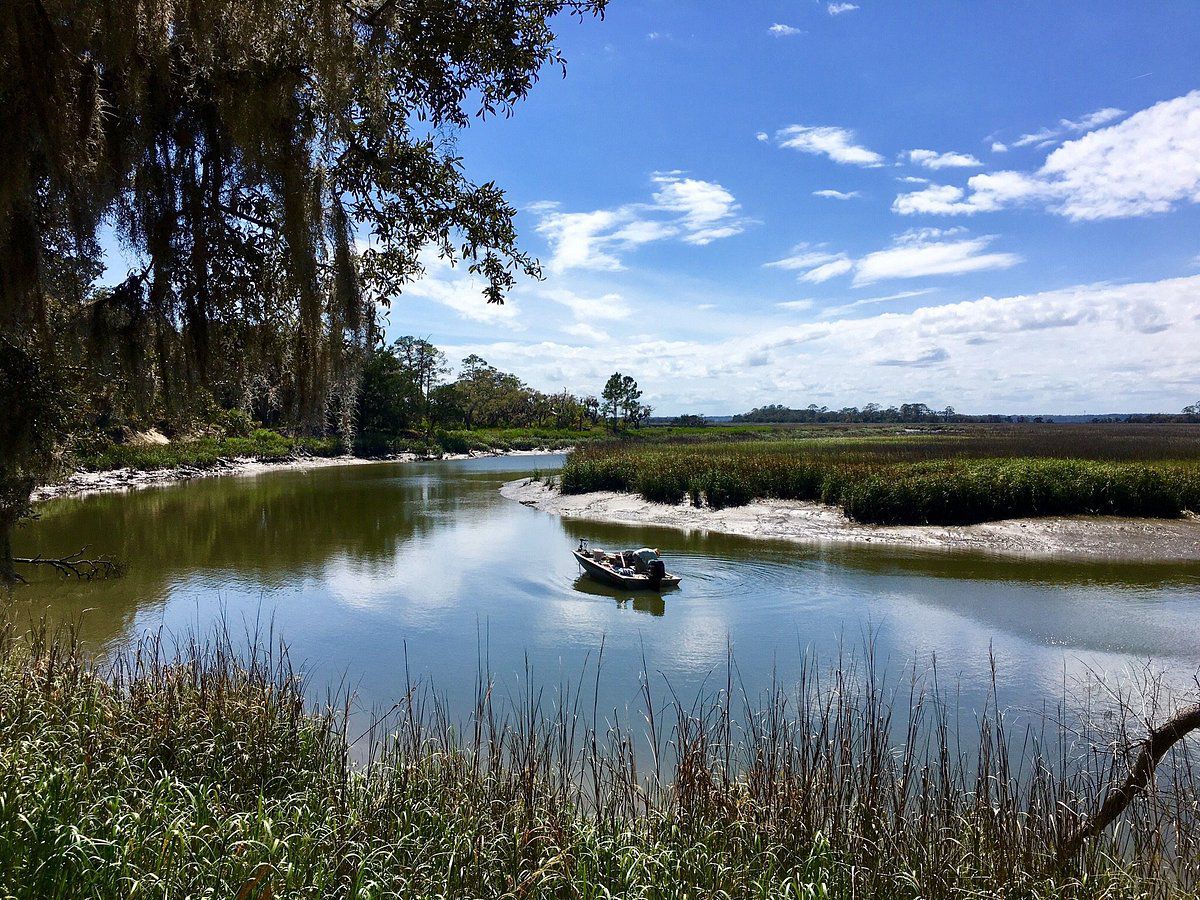 Small boat going around a bend in a river under sunny sky in rural landscape..