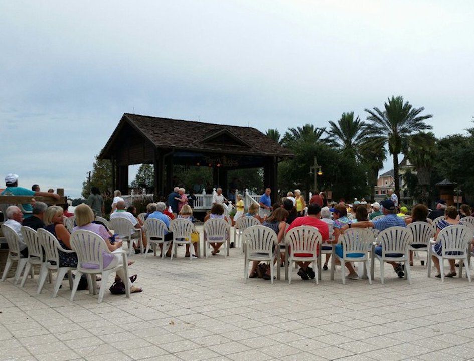 People sitting in white plastic chairs watching a show under an overcast sky at The Villages, Sumter County