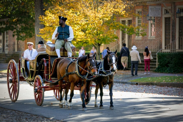 Williamsburg, Virginia, USA - October 23, 2024: A carriage drive chats with riders on Duke of Gloucester Street in the colonial historic district.