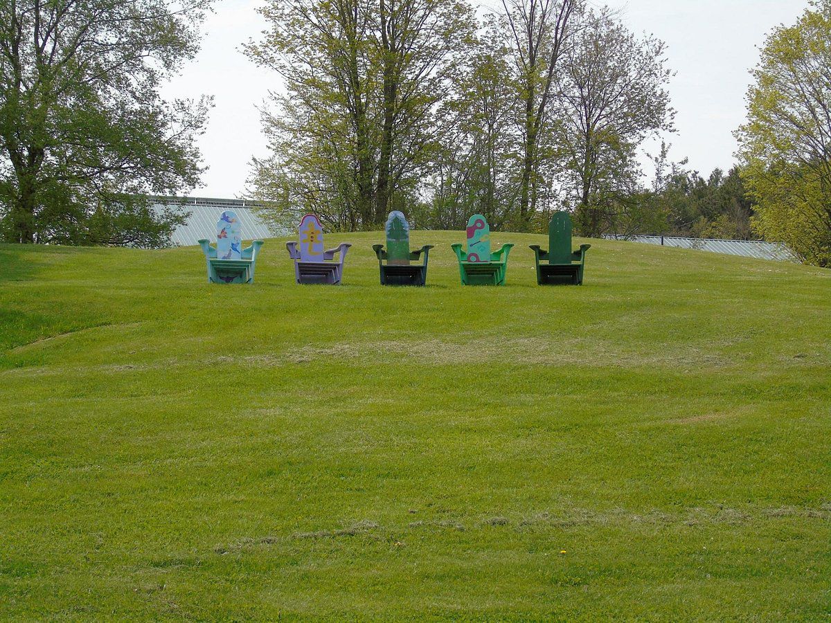 Five colorful wooden lounge chairs on a green hill on a spring day.