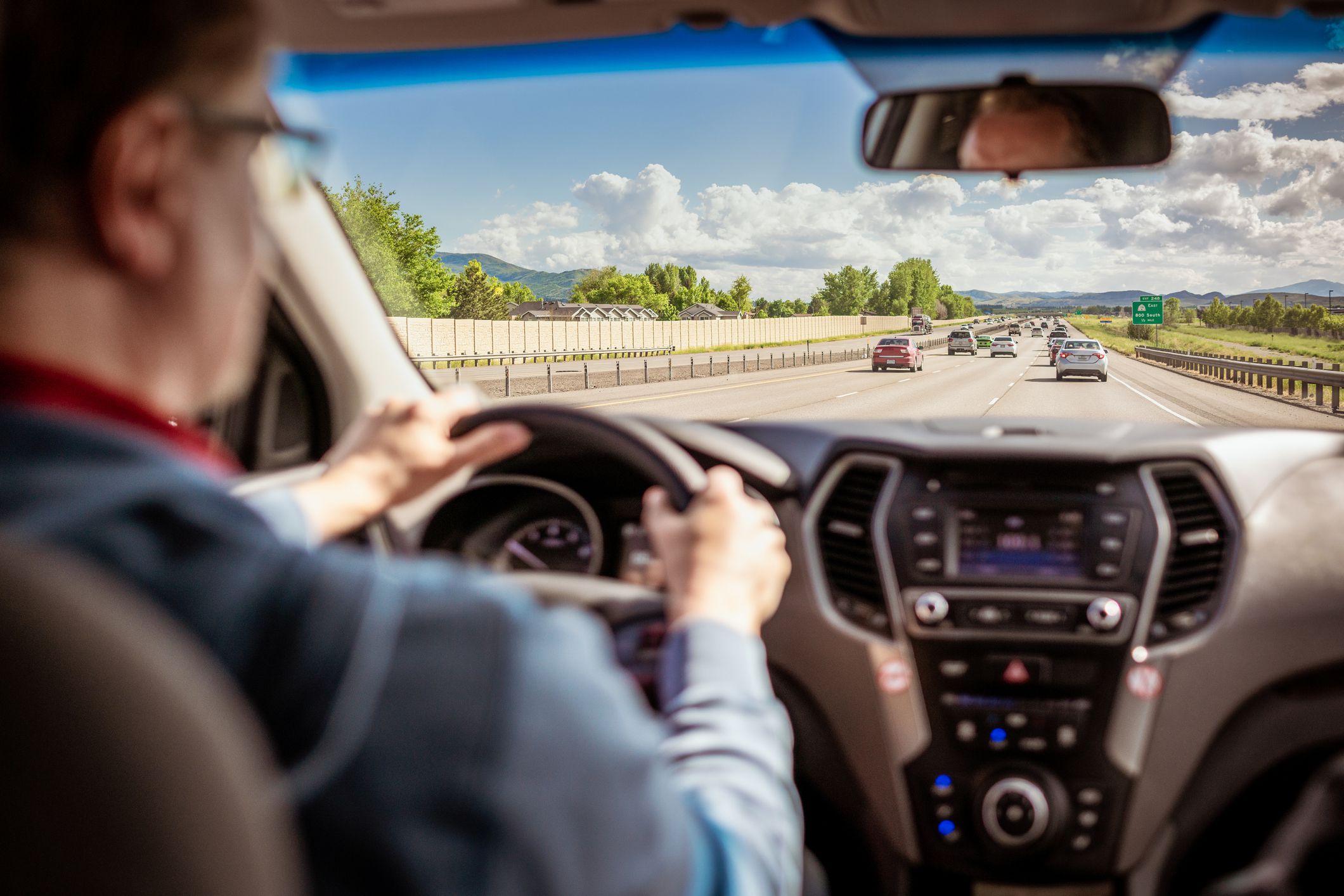 A man and the dashboard of his car defocused in the foreground, with light daytime traffic on a Utah Interstate highway in the distance.