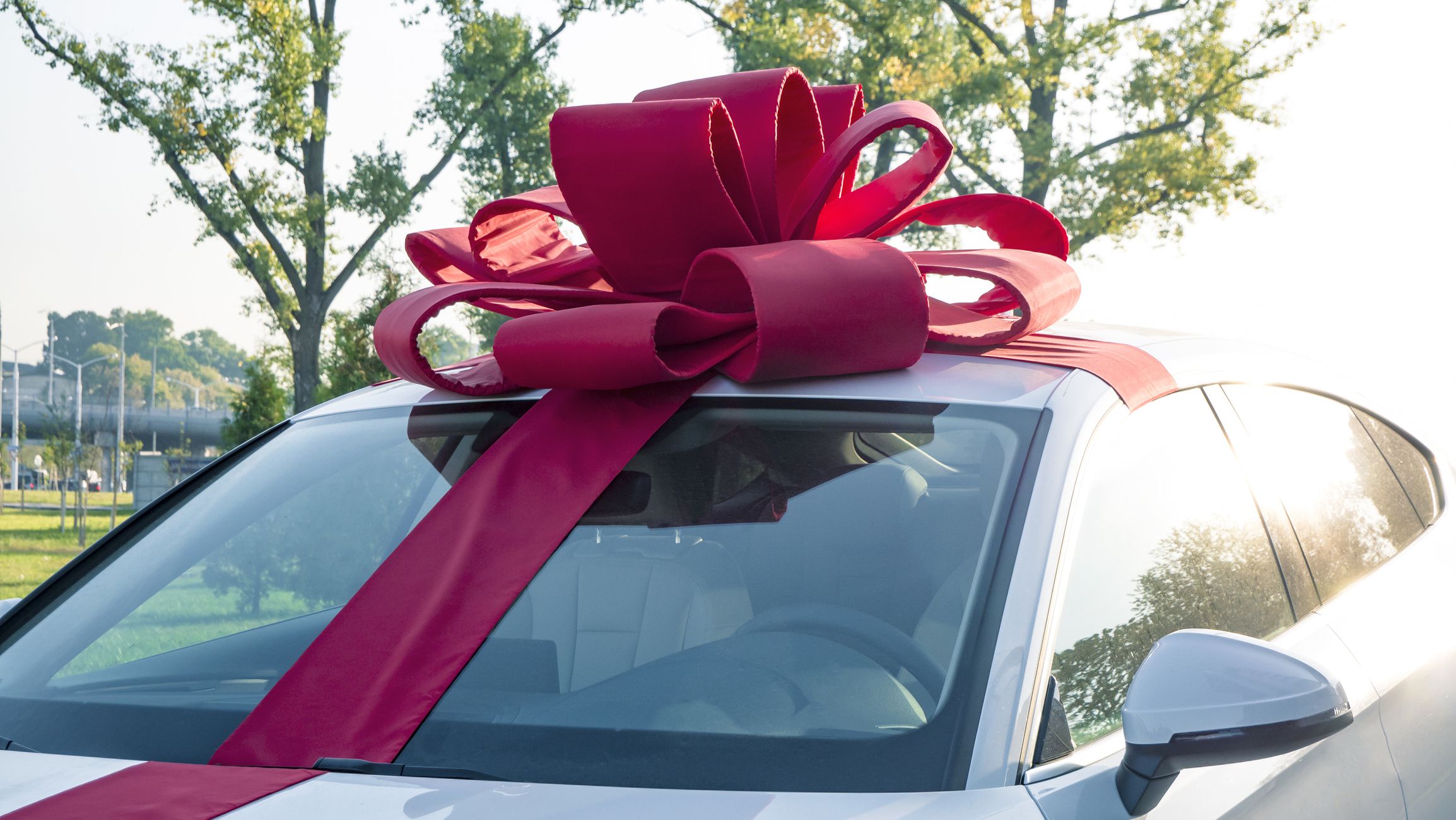 New car gift. New white car with red gift ribbon and bow awaits its buyer in the cabin. Auto dealership and rental concept background.