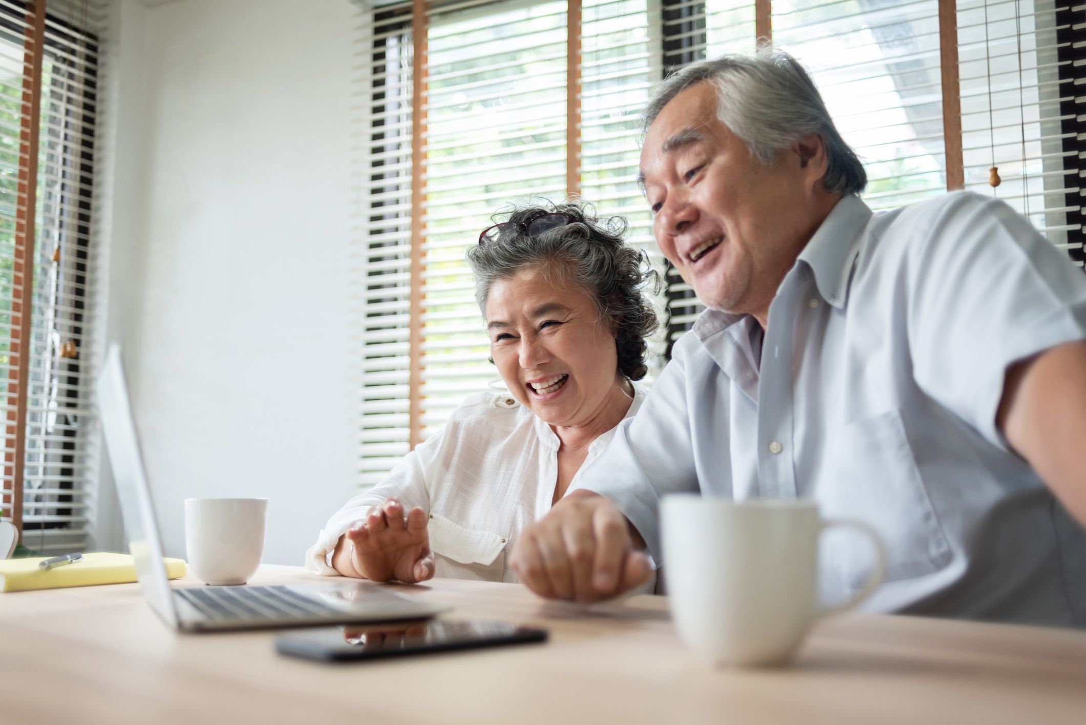 Cheerful Asian Senior couple having video chat with their family on Laptop computer on table at home indoor.