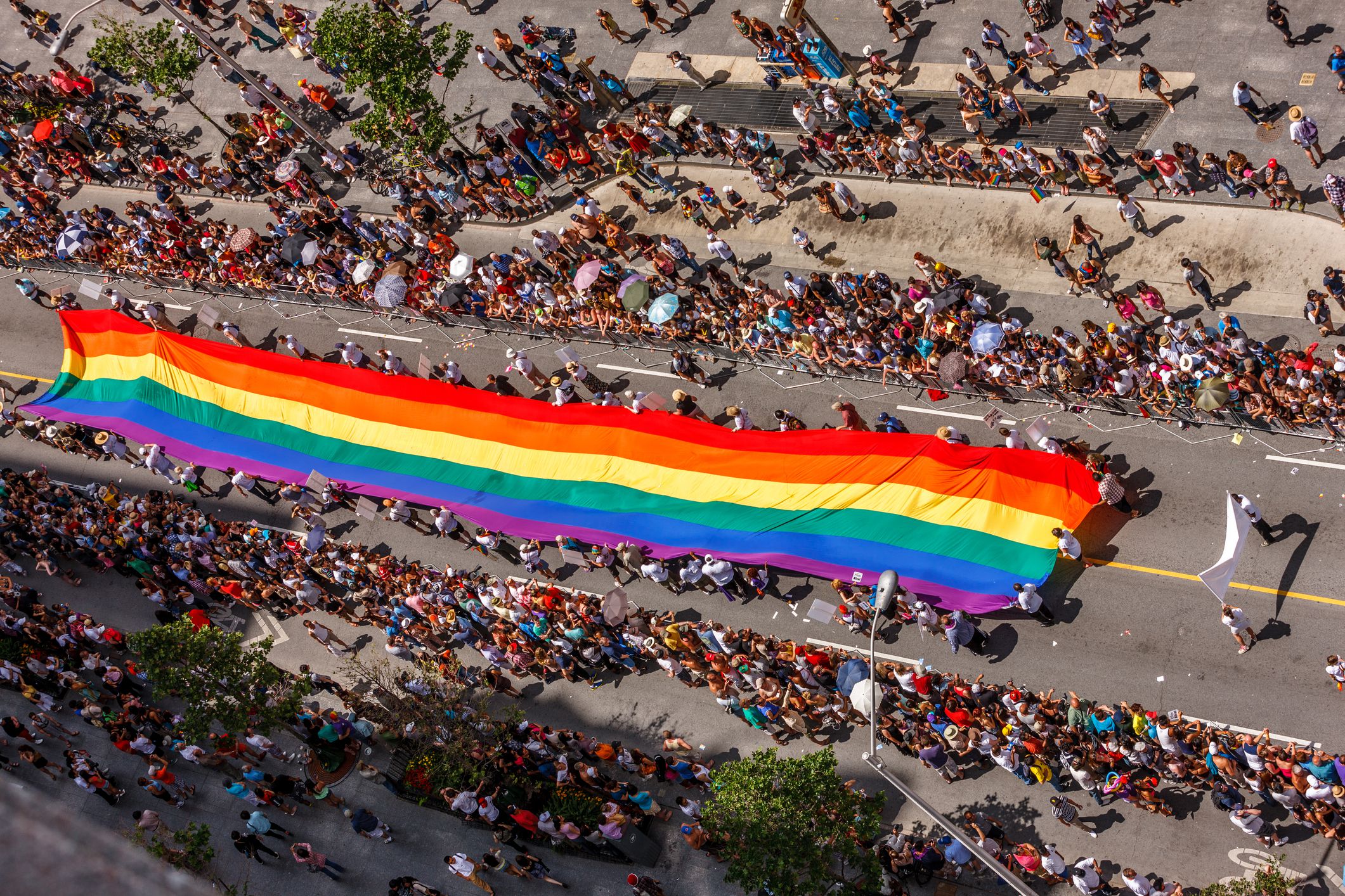 Toronto, Canada - July 3, 2011: Toronto Gay Pride Parade large multi-coloured flag in green, yellow and brown hues being carried along Bloor Street with cheering crowds either side
