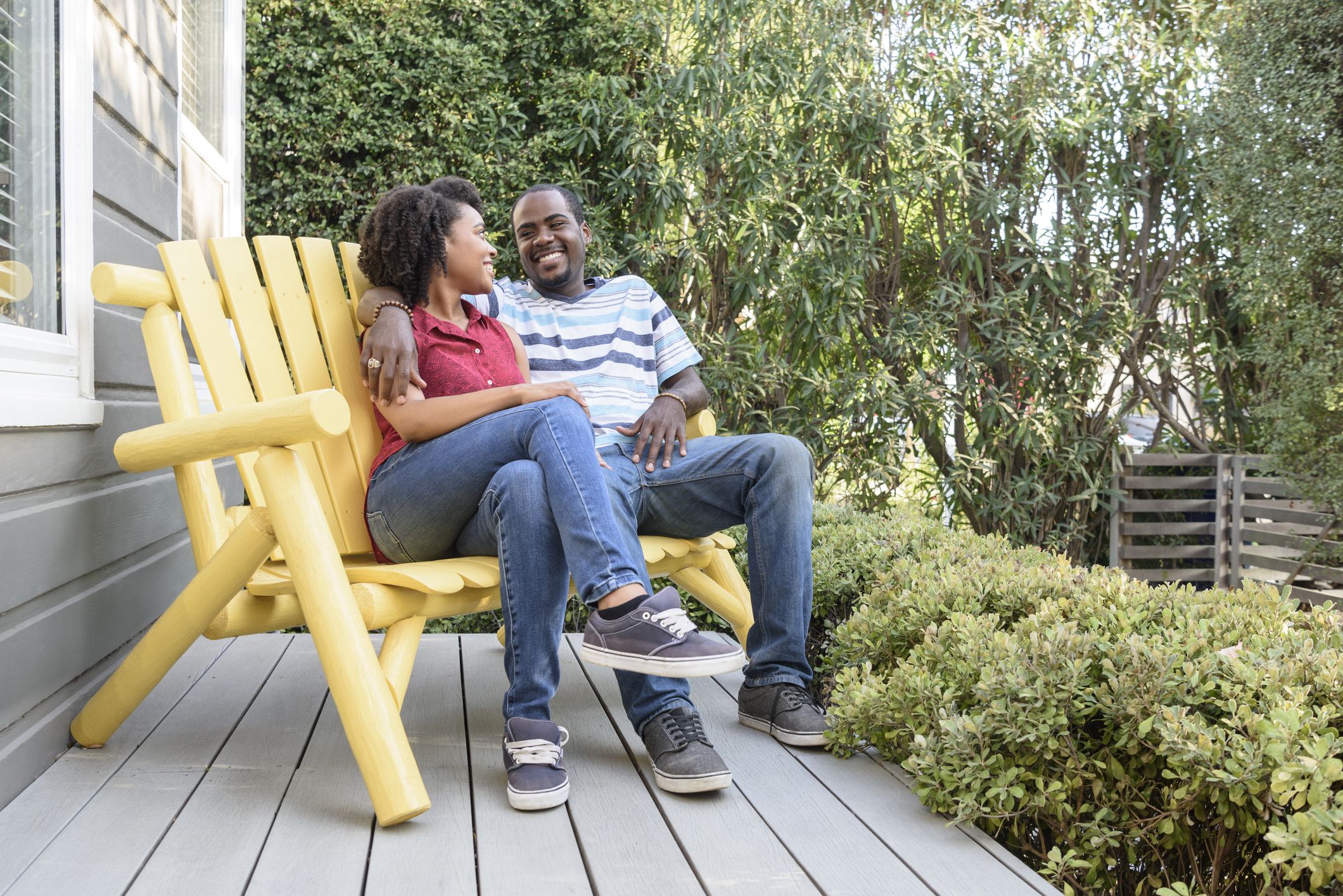 Young African American man with his arm around woman, they are smiling and sitting together on a yellow bench