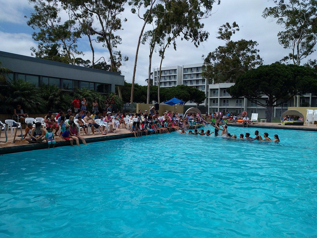 Kids playing in large swimming pool with overcast sky.