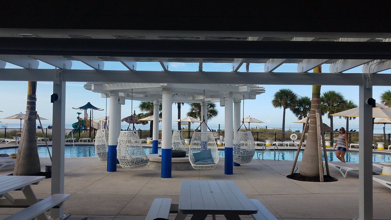 Hanging white lounge chairs under a cabana overlooking a pool and ocean.