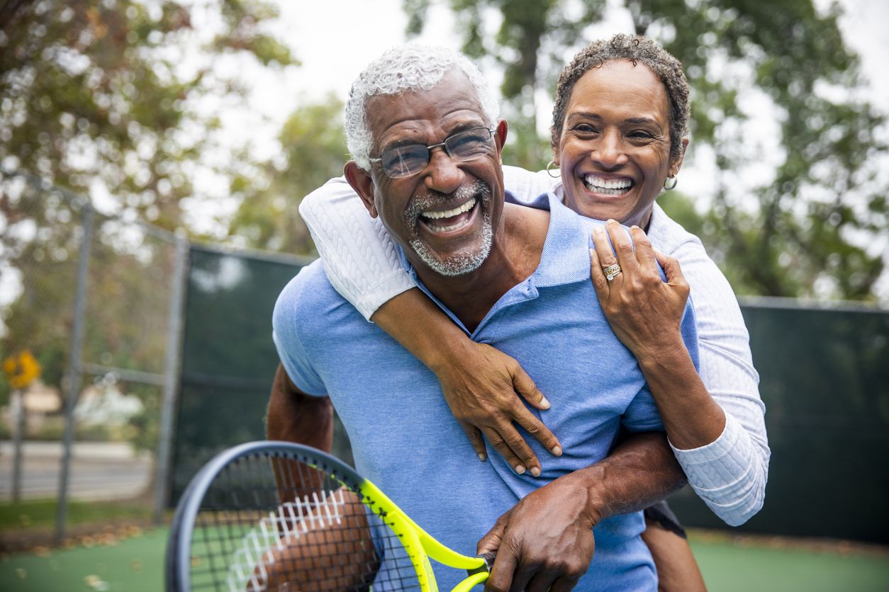 Laughing older couple hugging on a tennis court