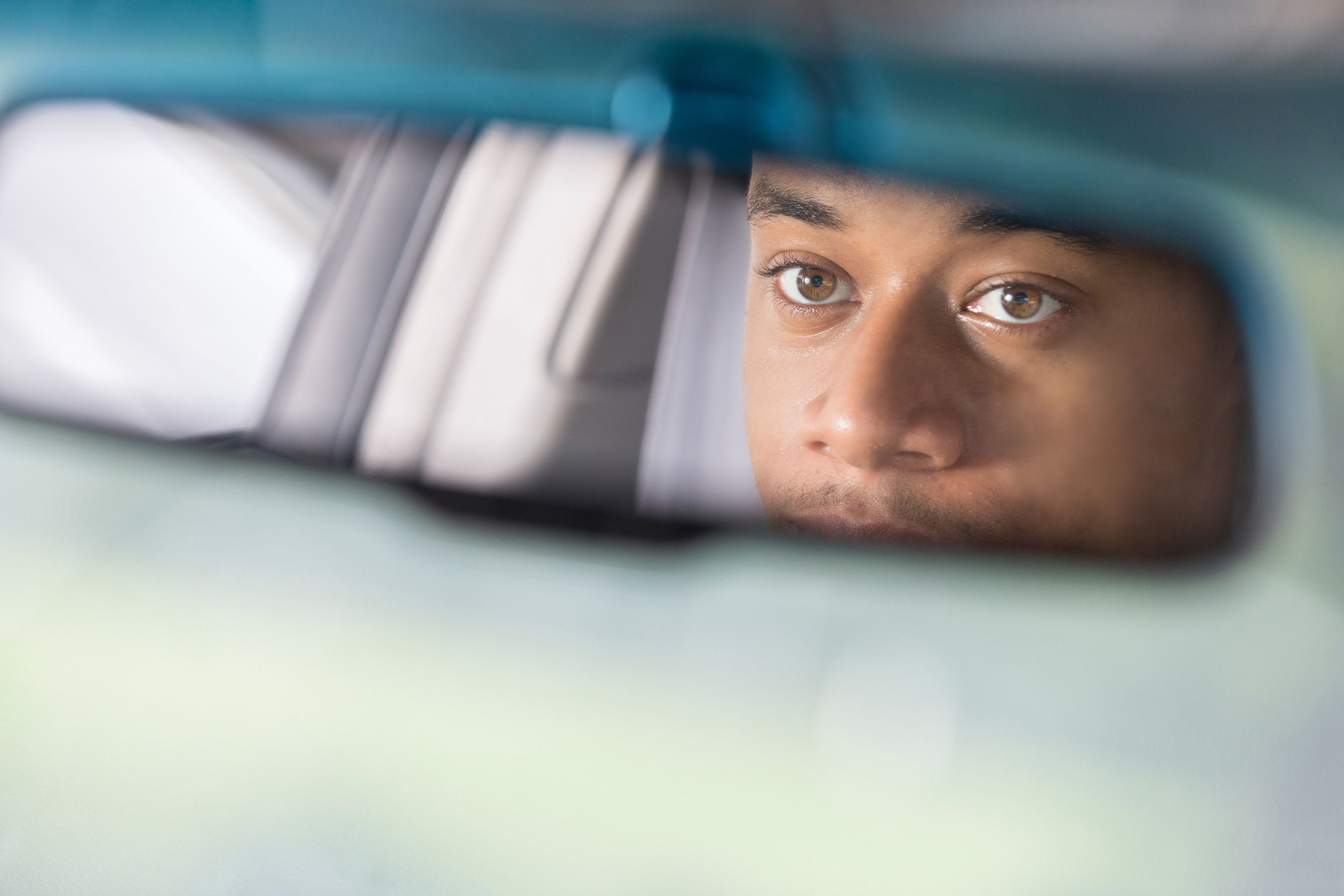 partial reflection of man looking in rear view mirror