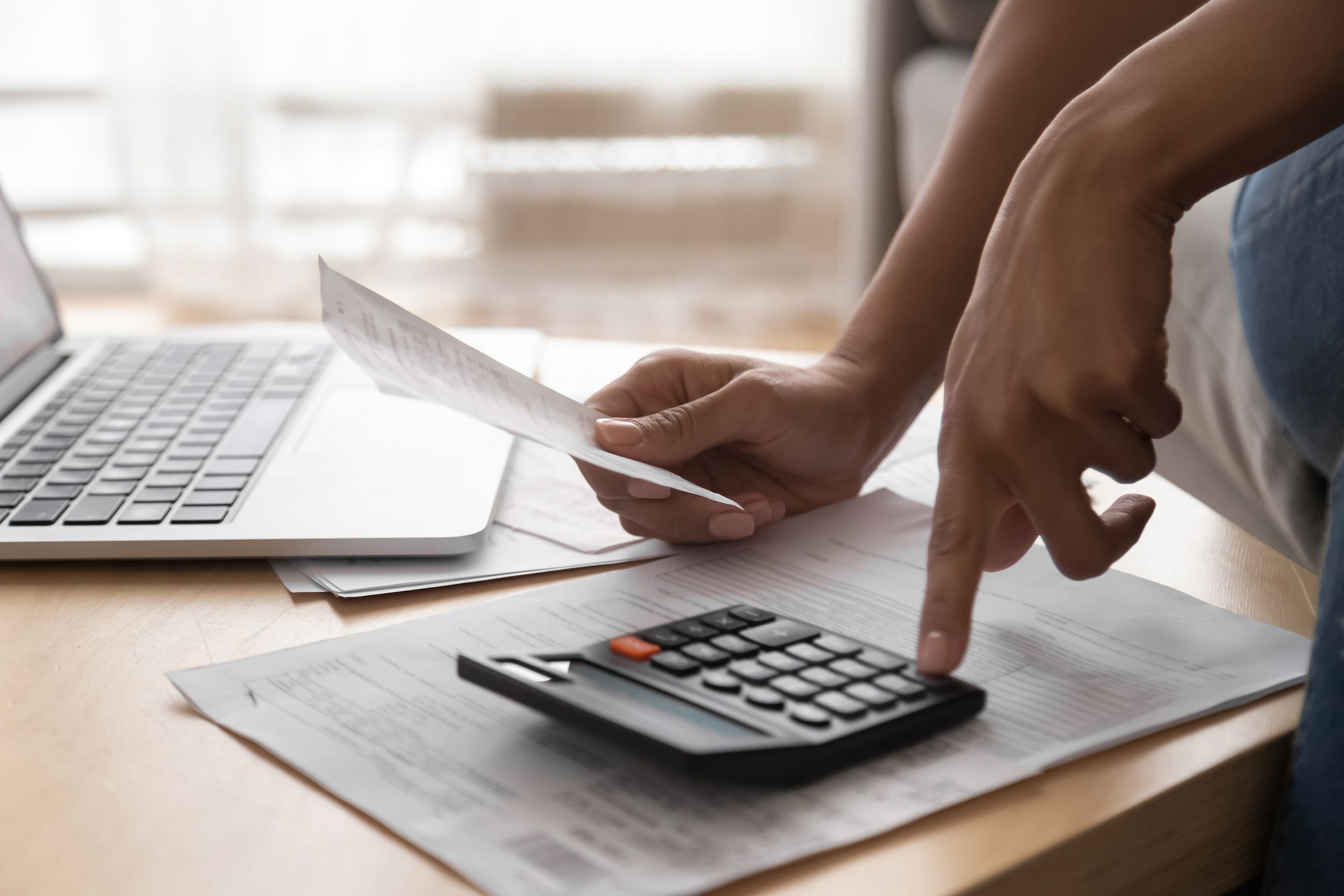 woman holding in hand paper bills bank receipt using calculator on table