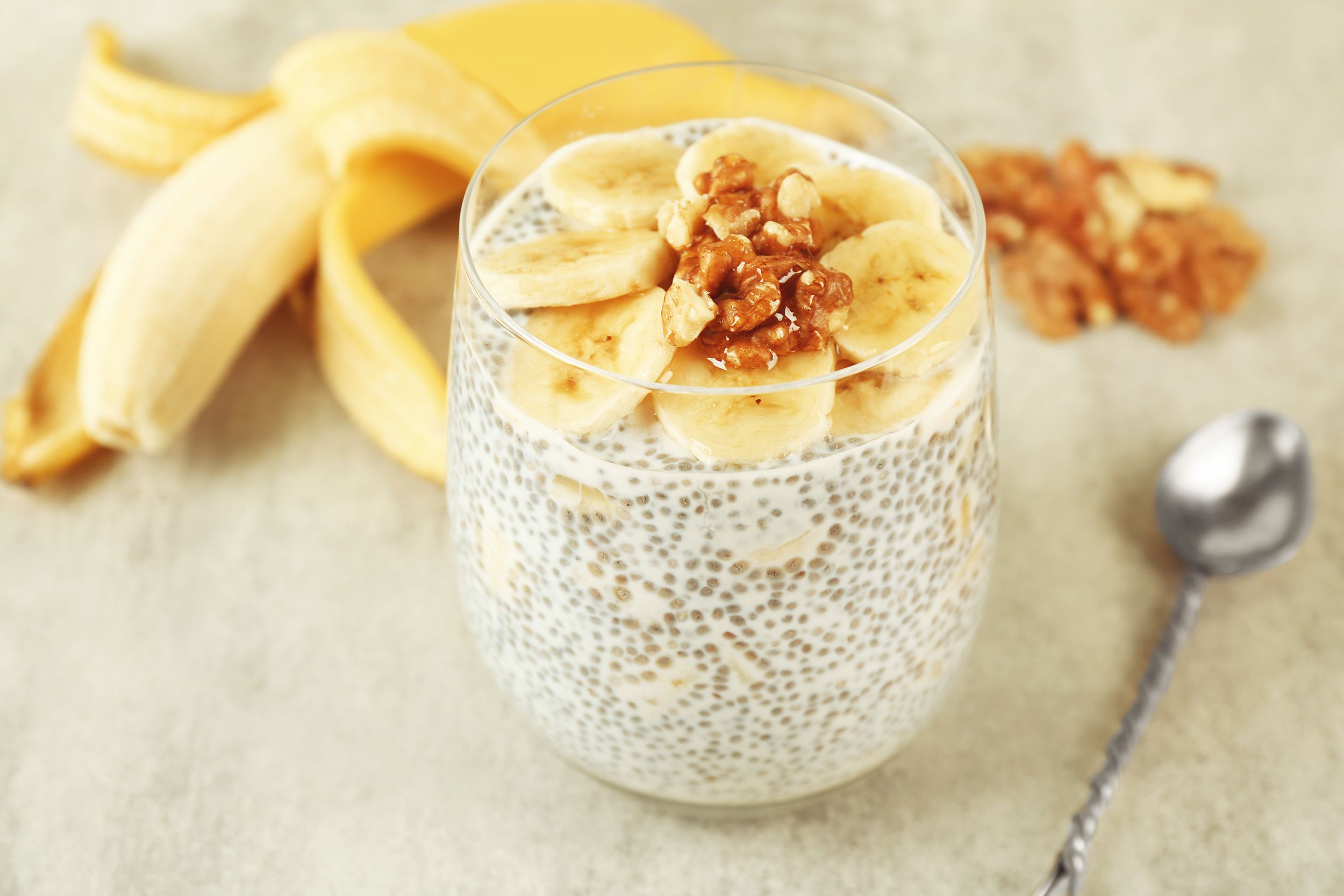 3-ingredient chia pudding in a glass dessert cup with a spoon, pecans, and a peeled banana in the background