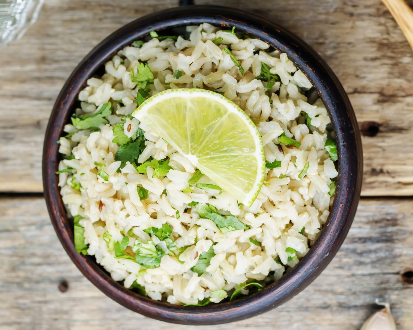 Closeup of 5-ingredient cilantro lime chicken and brown rice skillet in a brown ceramic bowl on a rustic wooden table
