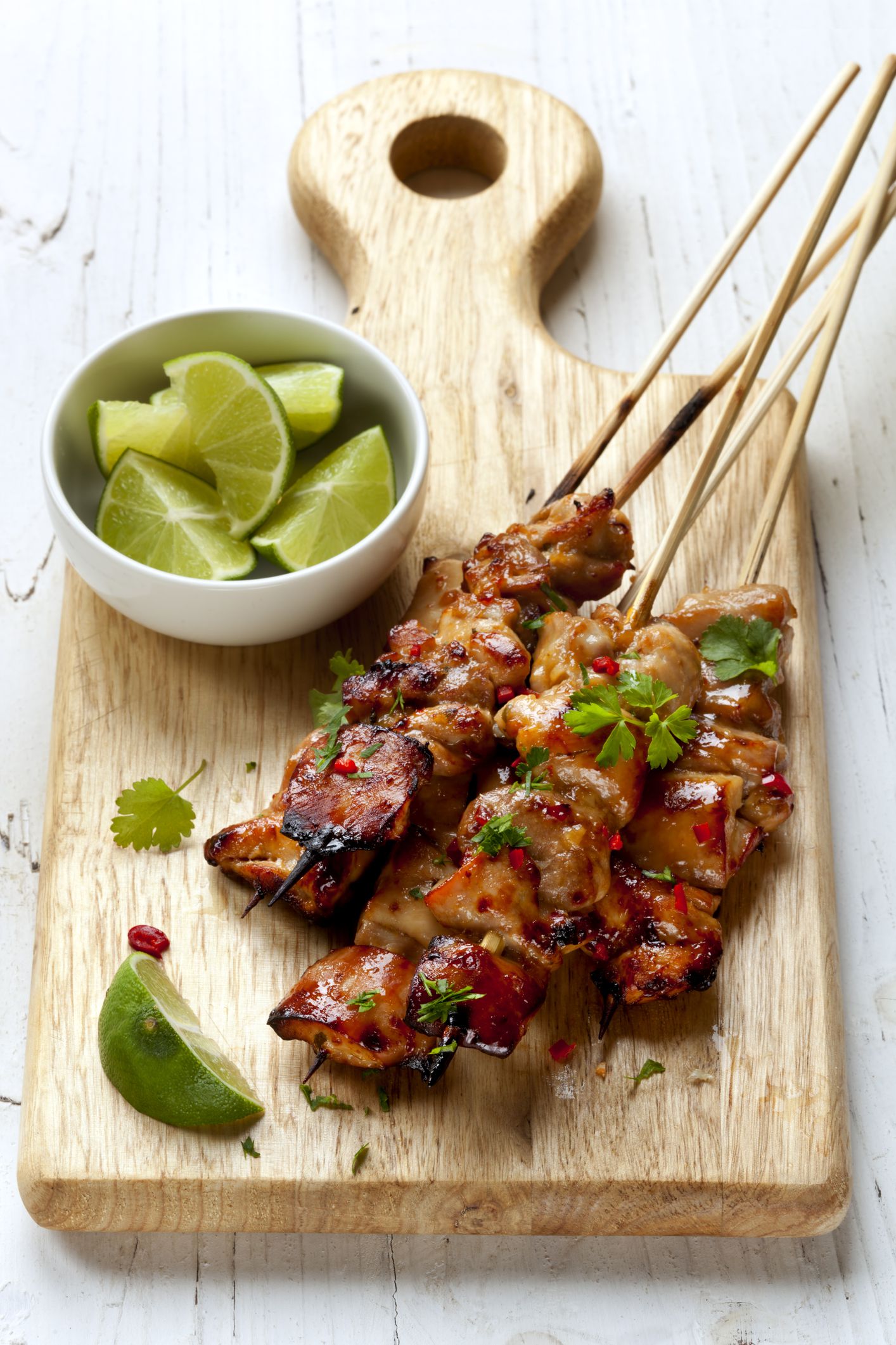 Closeup of 5 ingredient coconut curry kebabs on a wooden serving board with a bowl of limes on a a white wooden table