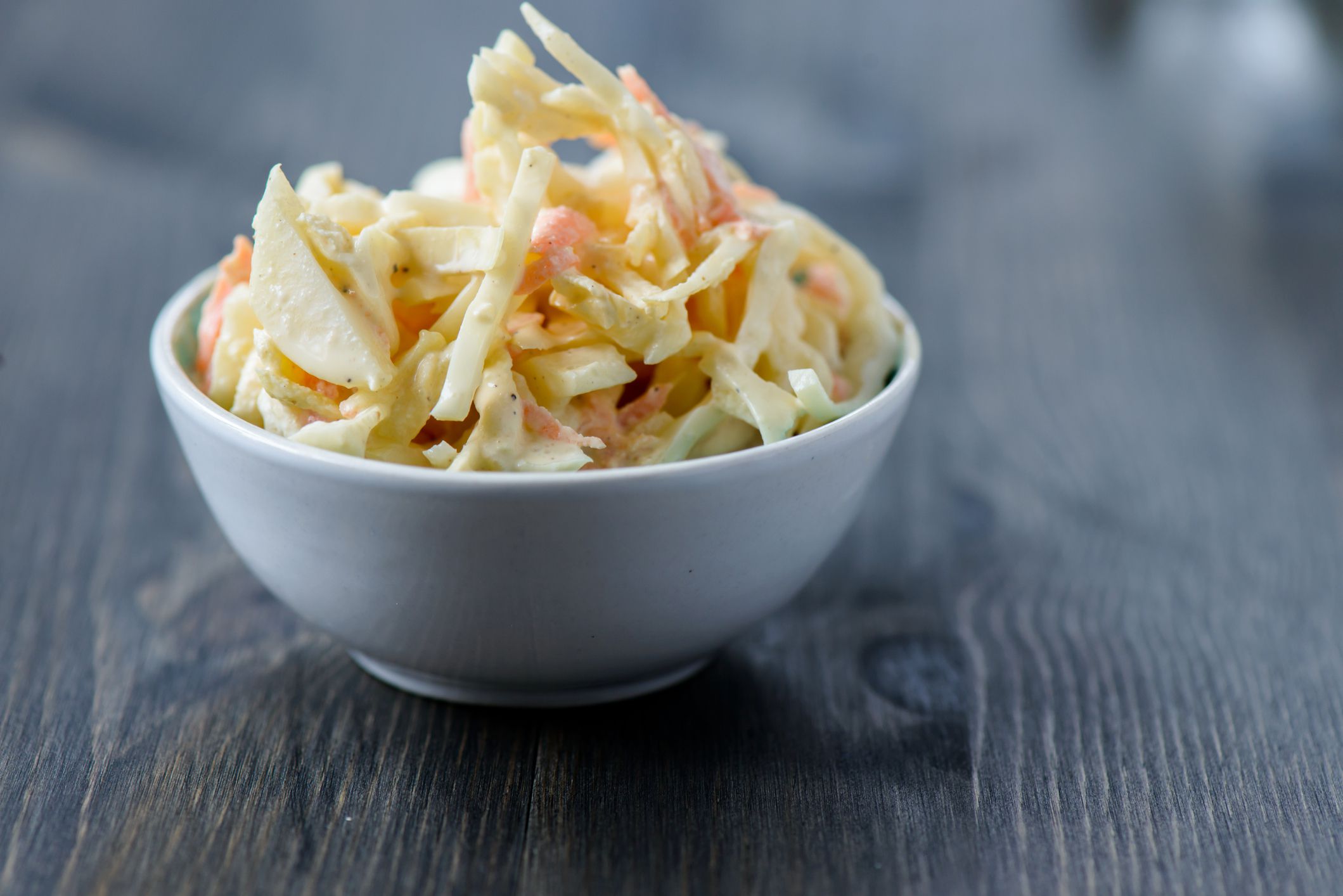 Closeup of 5 ingredient coleslaw in a grey ceramic bowl with a blurred background of a dark grey wooden table