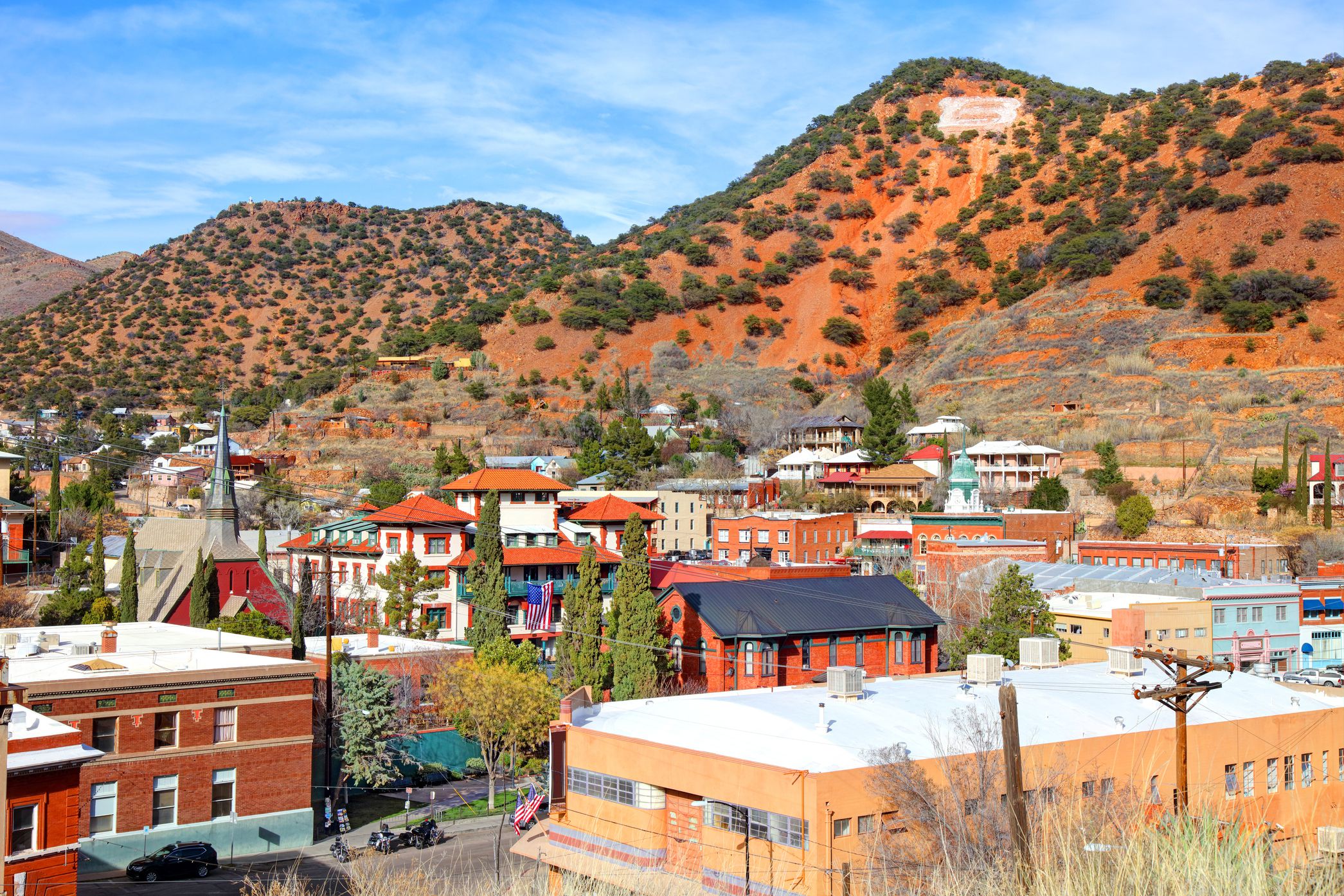 Aerial of buildings of downtown Bisbee, Arizona with red Mule Mountains in the background, during winter with no snow on a sunny day