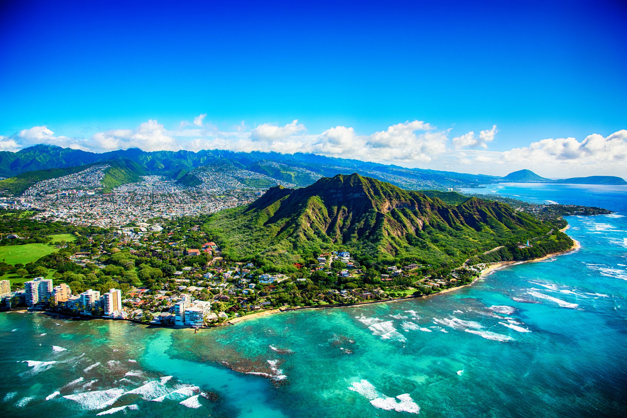 Aerial of Diamond Head and the Gold Coast neighborhood with surrounding areas in Oahu, Hawaii with beaches and ocean during a sunny day, clouds around the mountains in the background
