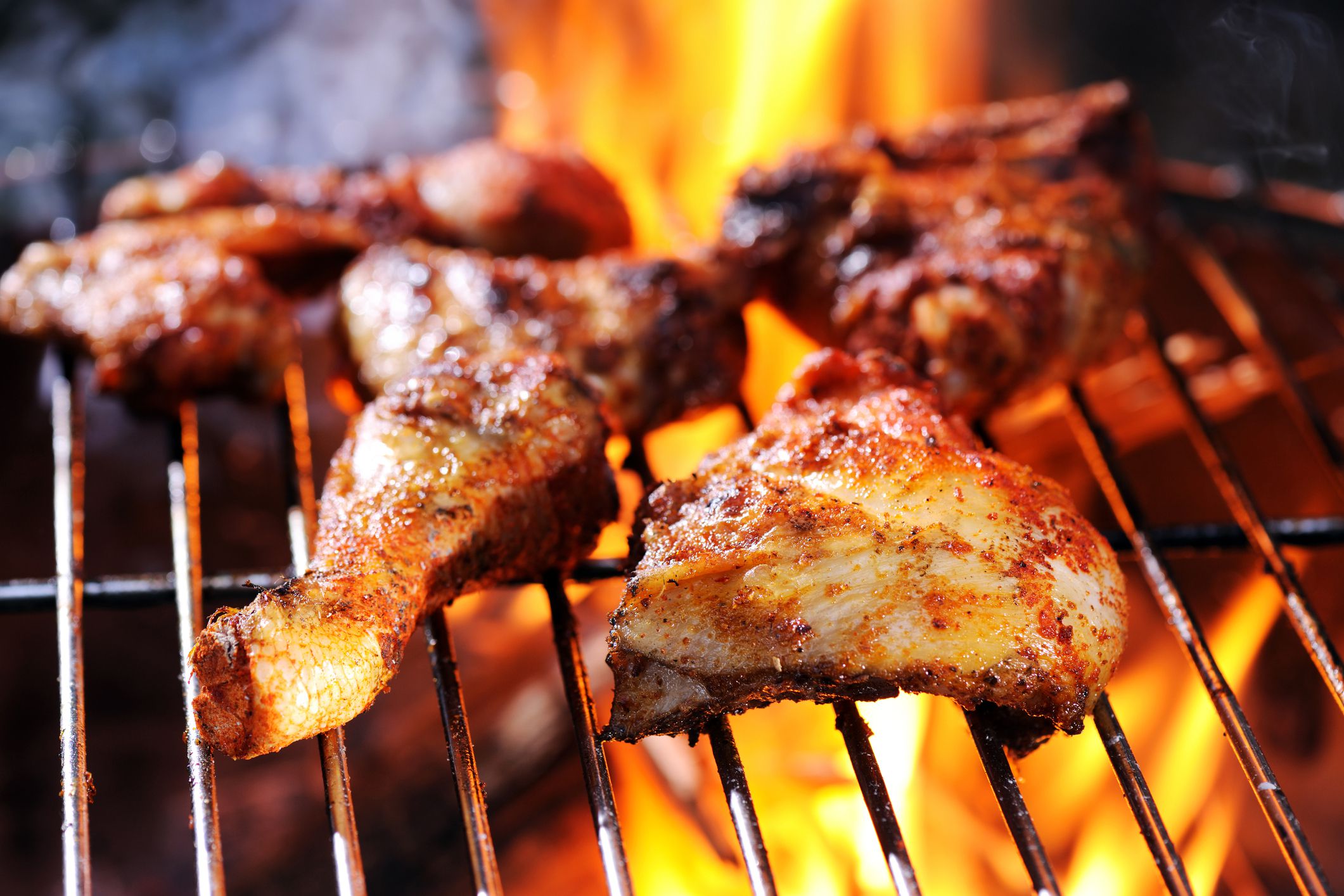 Closeup of pieces of BBQ chicken on the grill with grill flame in the background