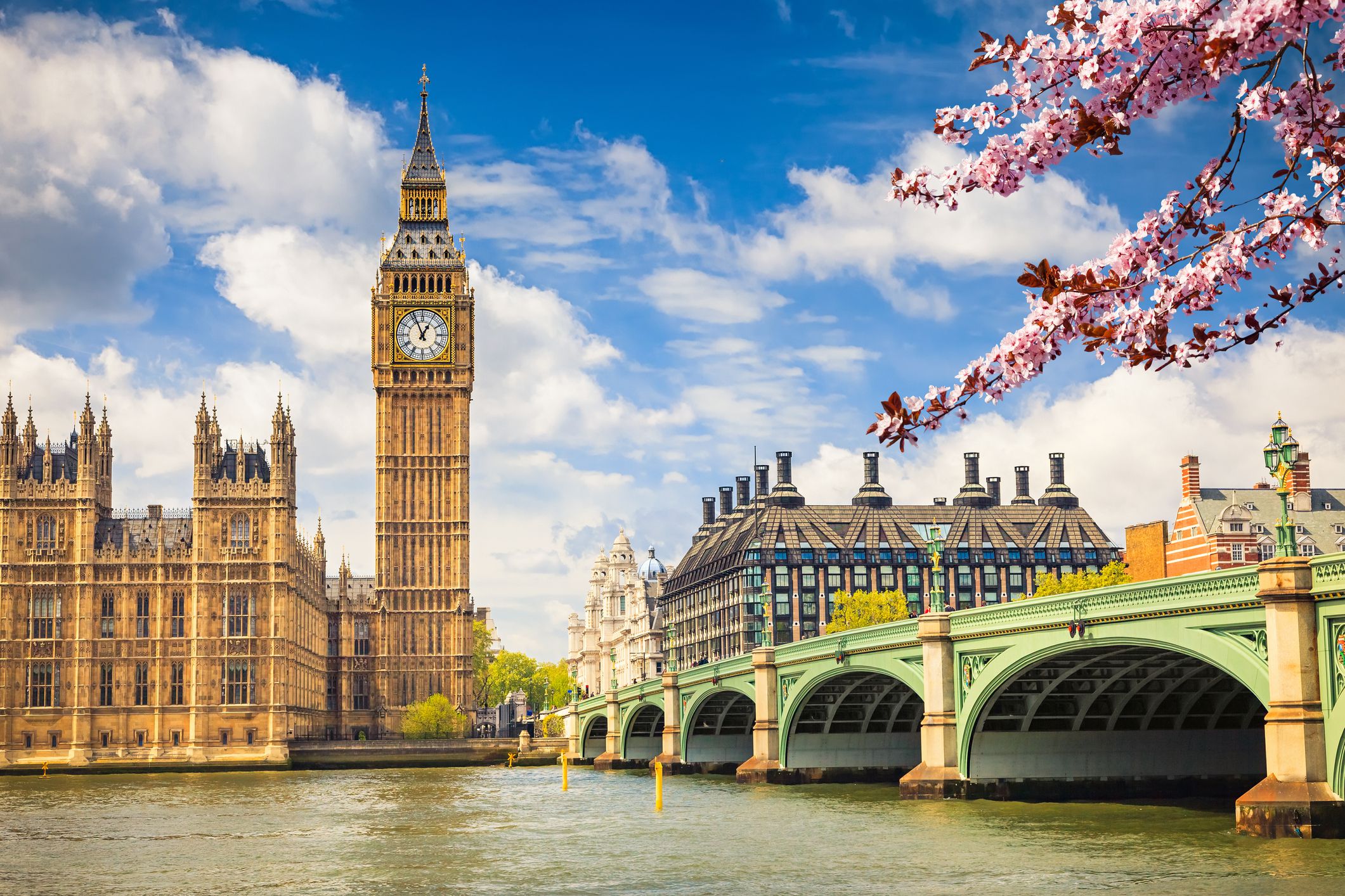 Big Ben and Westminster Bridge in London during spring, river thames in the foreground, a bright blue sky with white clouds