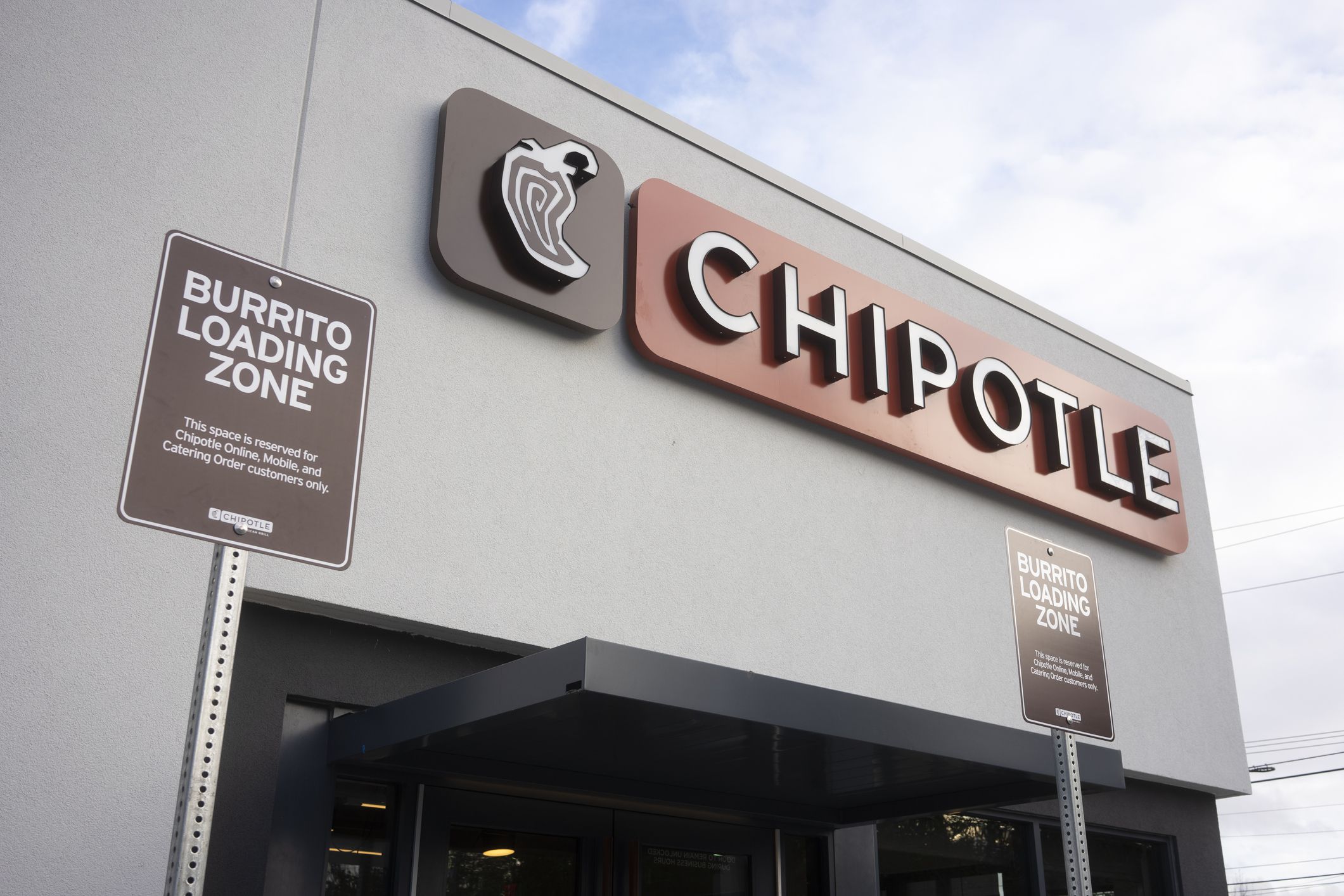 Closeup of the Burrito Loading Zone Parking Signs near the entrance of a Chipotle Mexican Grill in Portland, Oregon with a blue and white cloud sky in the background