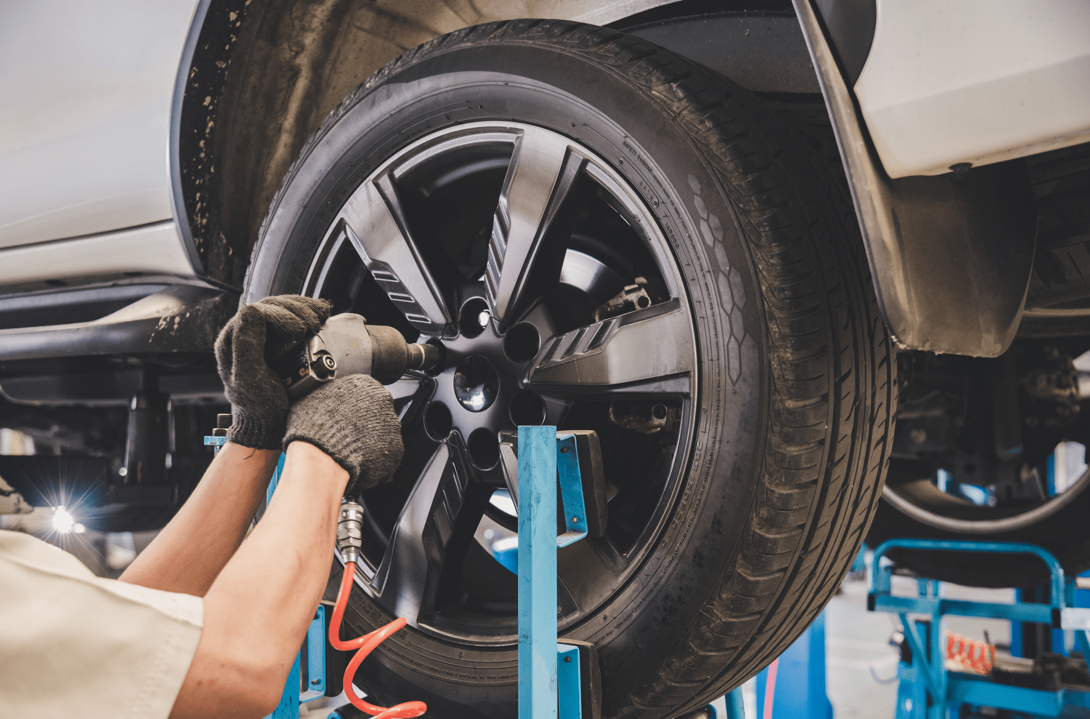 Car mechanic putting the bolts of a new tire in of an elevated car, inside a repair garage