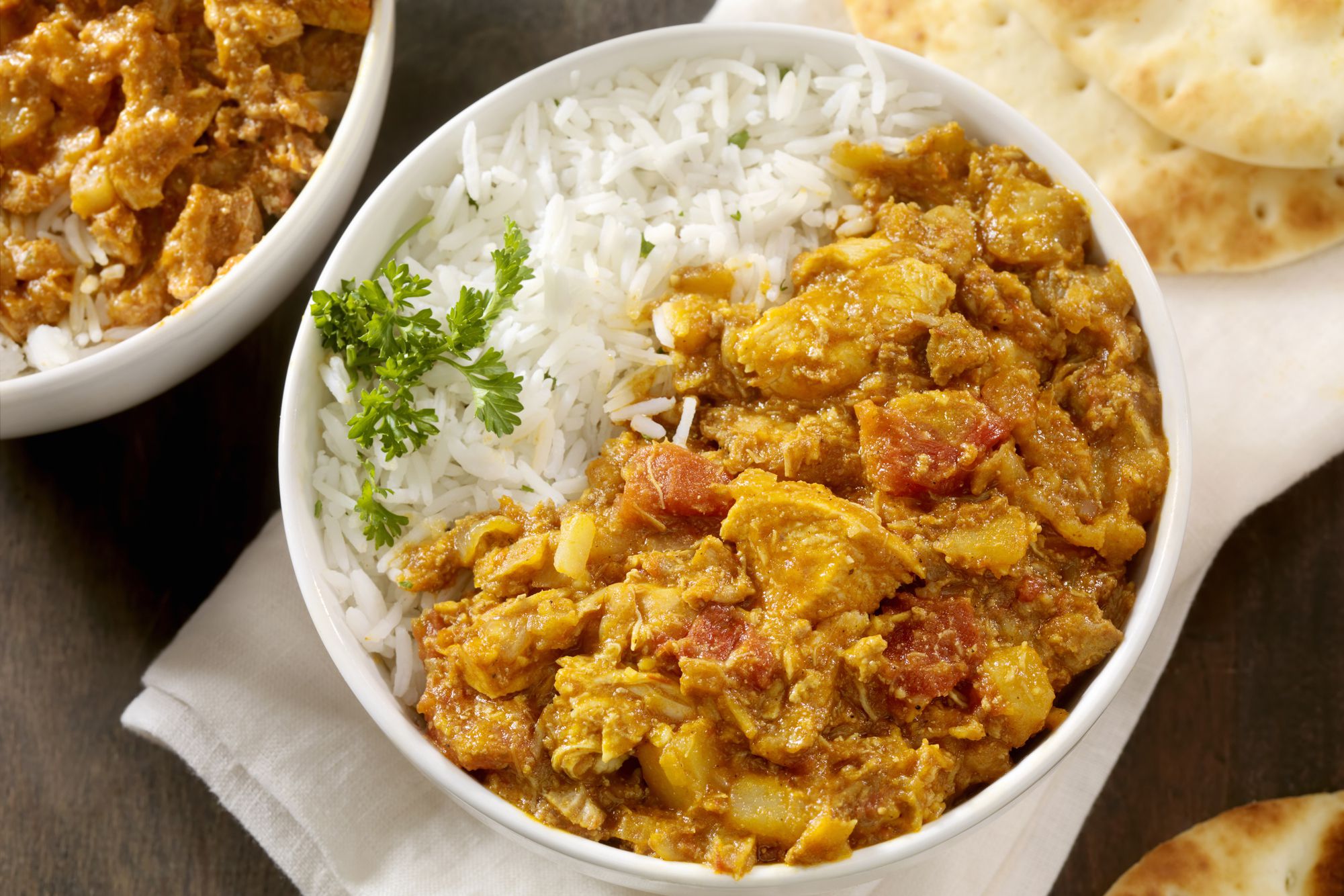 Chicken tikka masala with rice in a white bowl on a white napkin with naan and another serving