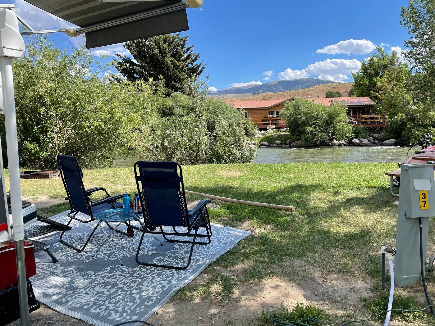 Dubois Wind River KOA, Dubois, Wyoming, looking out from an RV tent set up on an RV lot onto a river and a cabin with mountains in the background