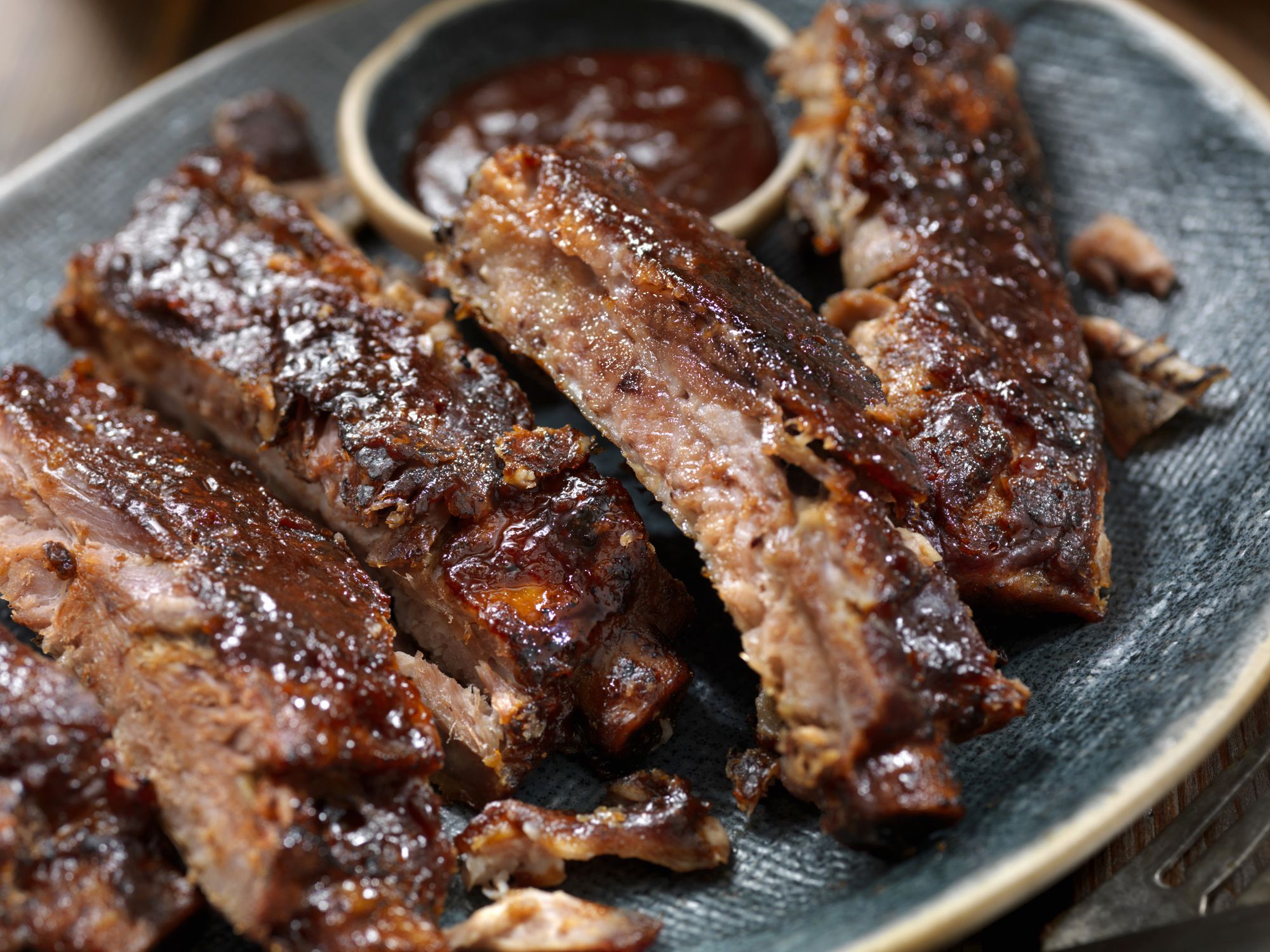 Easy slow cooker BBQ country-style ribs on a blue ceramic plate with BBQ sauce in the background