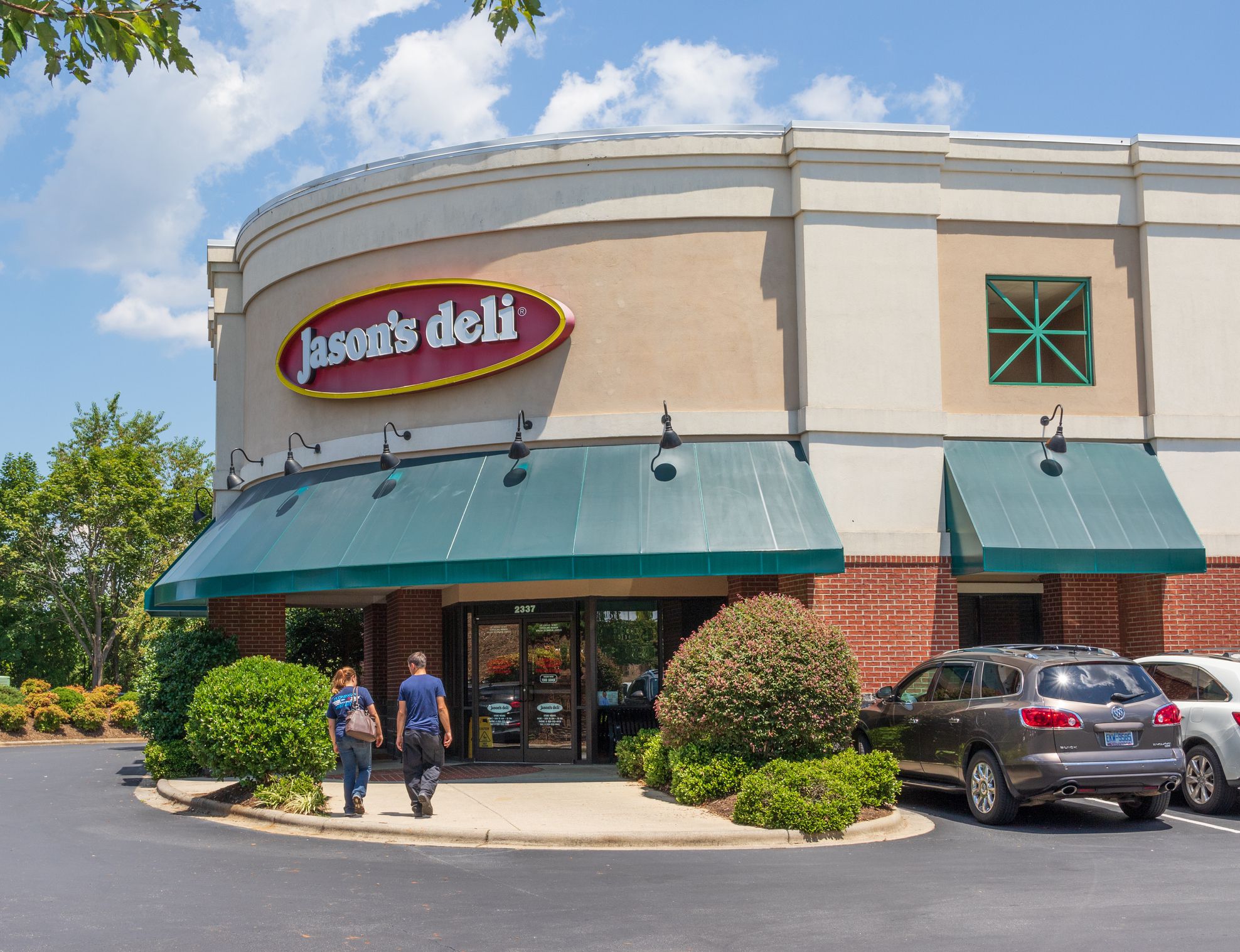 Exterior of a Jason's Deli in Hickory, North Carolina with two people walking toward it on a bright, sunny day