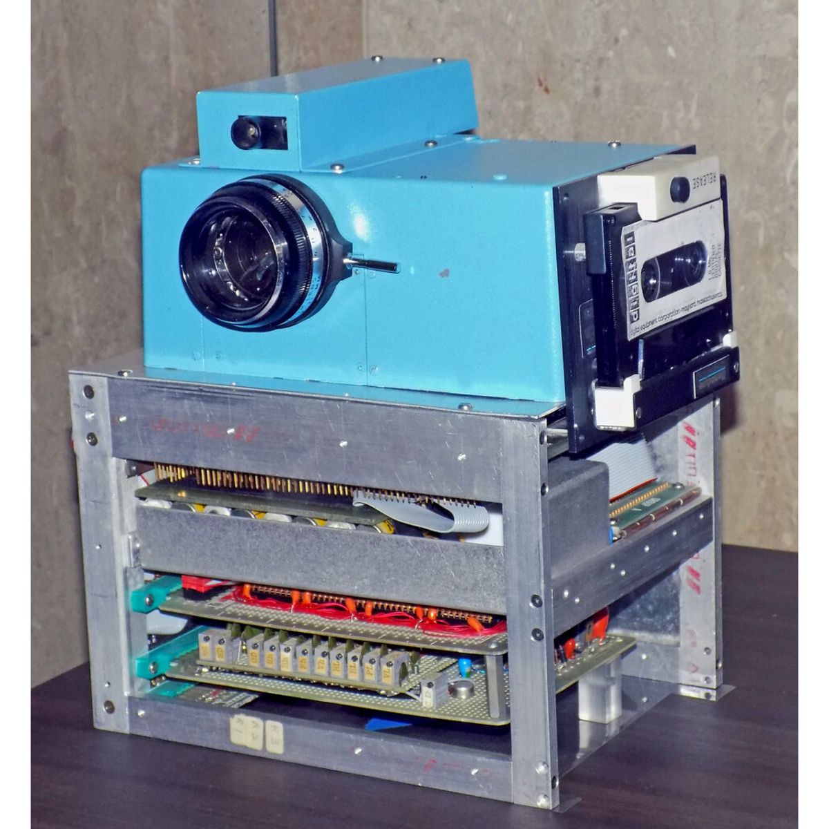 First digital camera on a table with a rustic wall in the background
