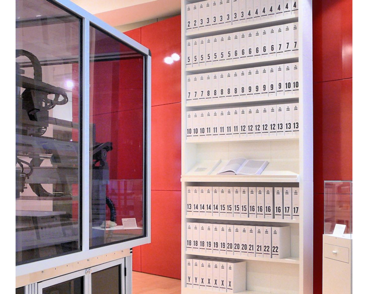 First printout of the human genome displayed in a series of books at the Wellcome Collection, London, lab items on the right, and a red walled background