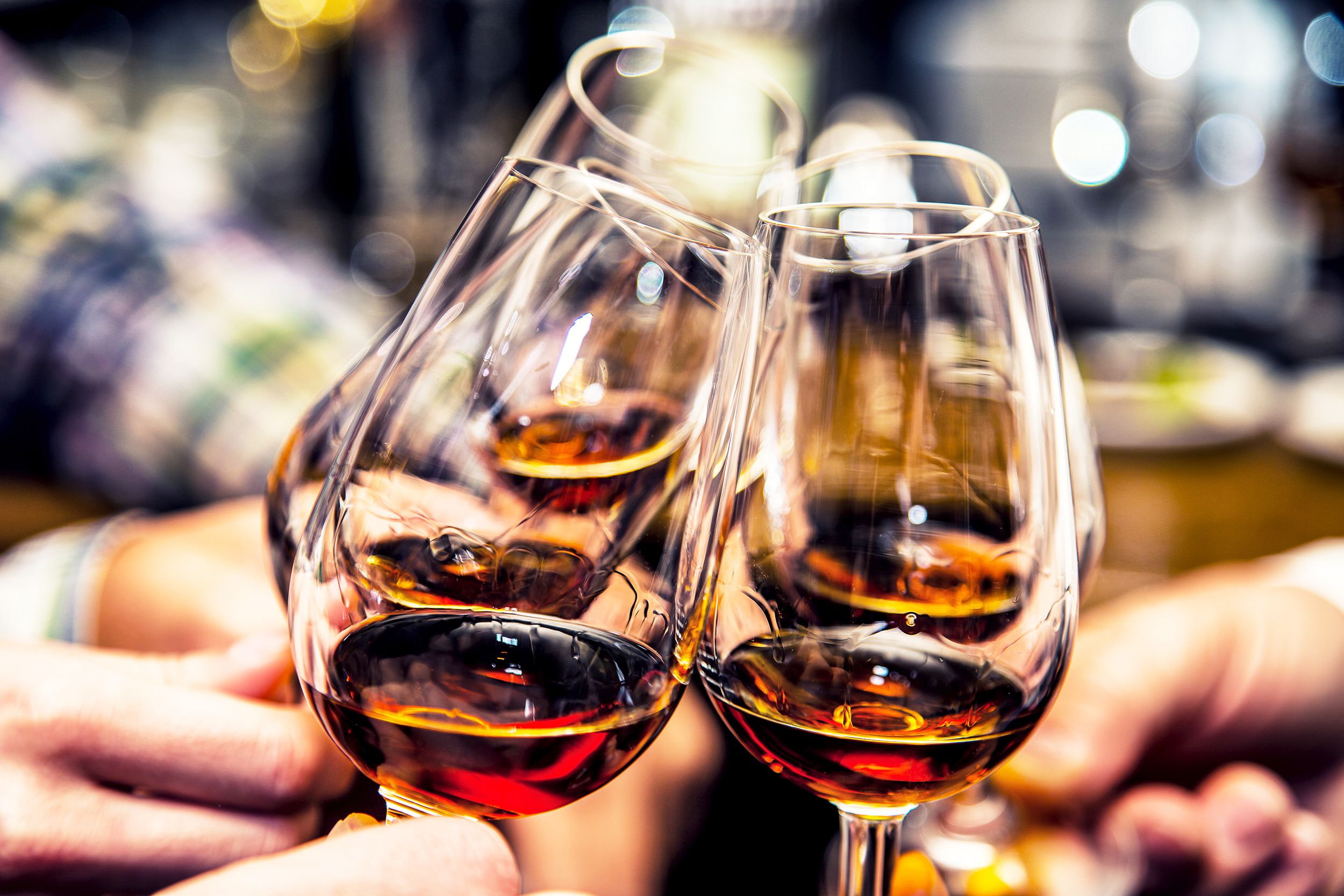 Five wine glasses being toasted, held by hands, selective focus, blurred surrounding of arms at a bar
