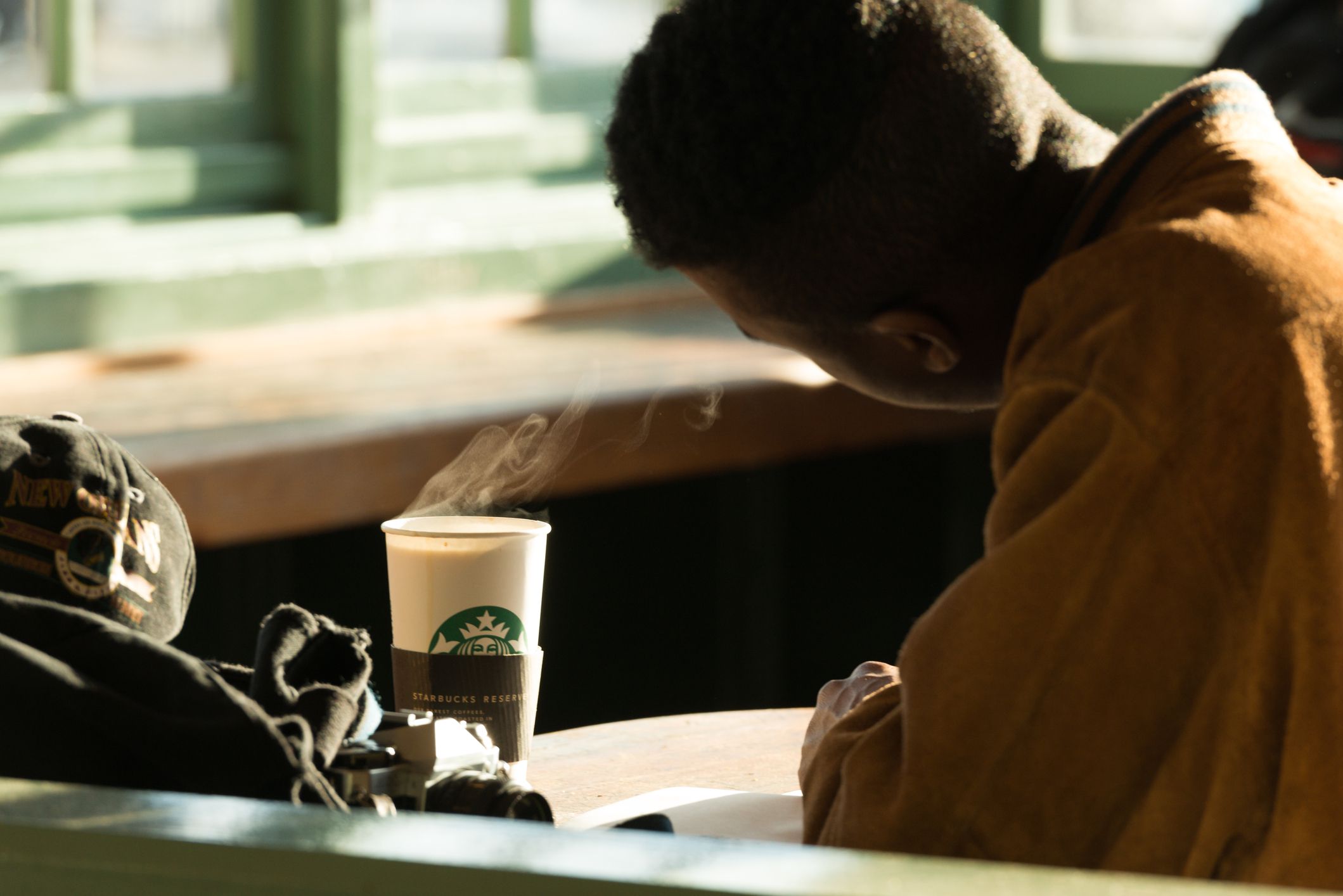 Focus on a hot cup of Starbucks coffee while a man is reading in a Starbucks in Pike Place Market, Seattle during early evening with sun at an angle