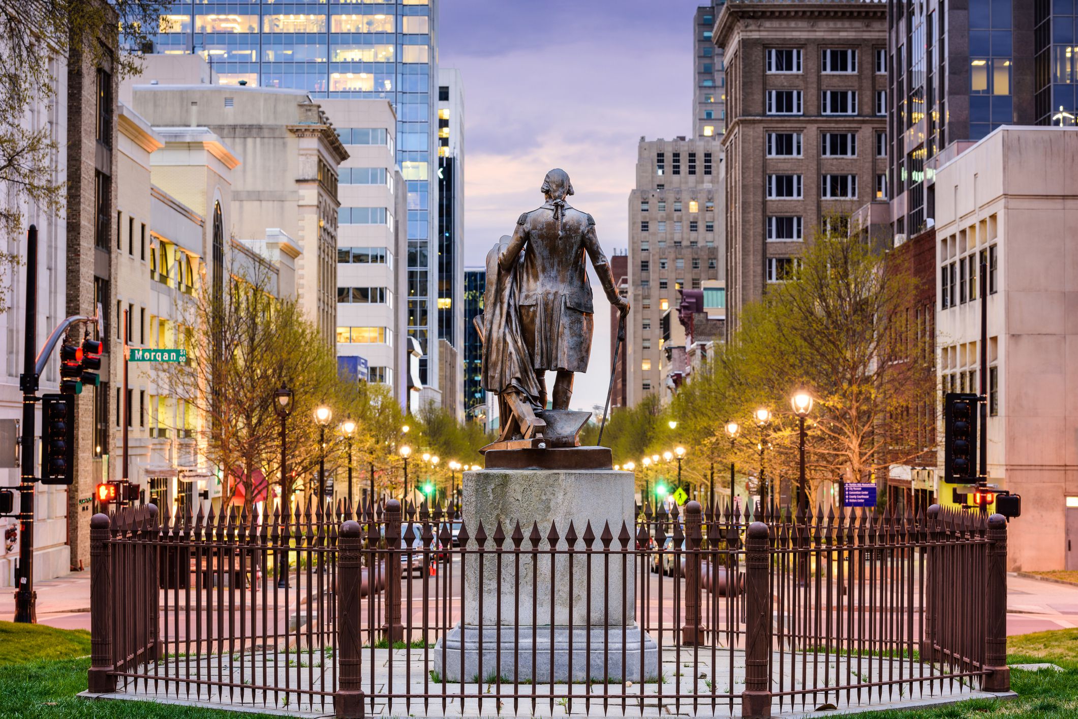 George Washington Monument as viewed from the Capitol building grounds in downtown Raleigh, North Carolina, late sunset during spring, downtown buildings in the background, lights on
