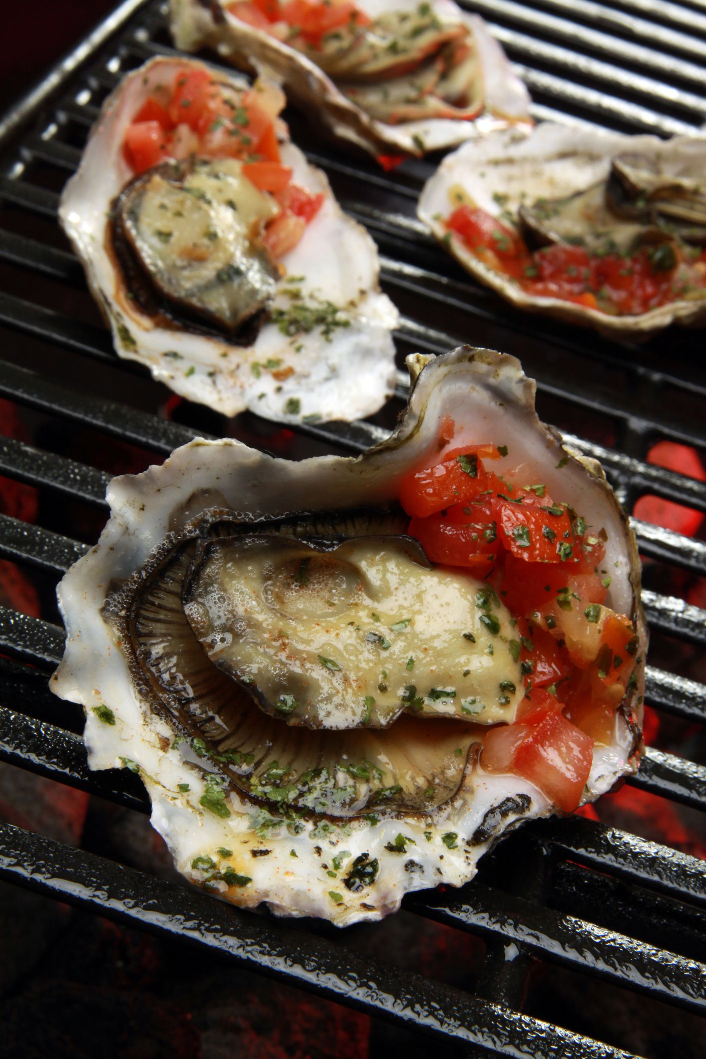 Closeup of four grilled oysters with chorizo butter on a grill