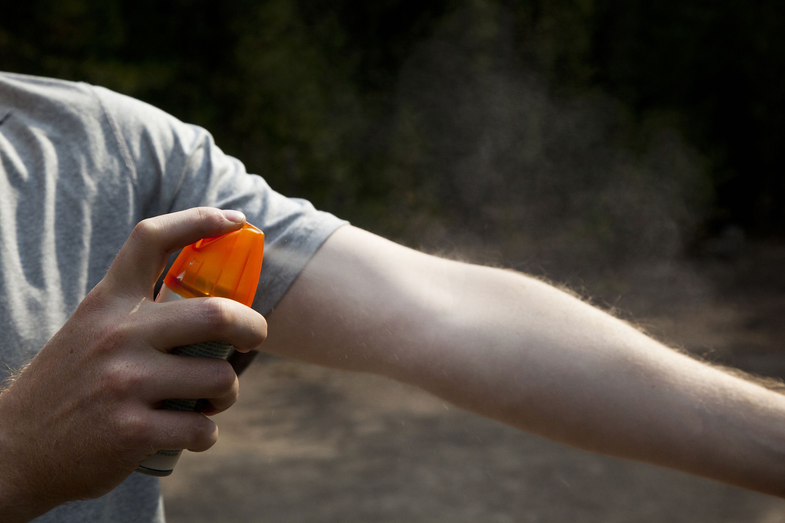 Man’s hand holding OFF! FamilyCare Insect Repellent spraying it on other arm, hand in the foreground, darkened brown blurred in the background