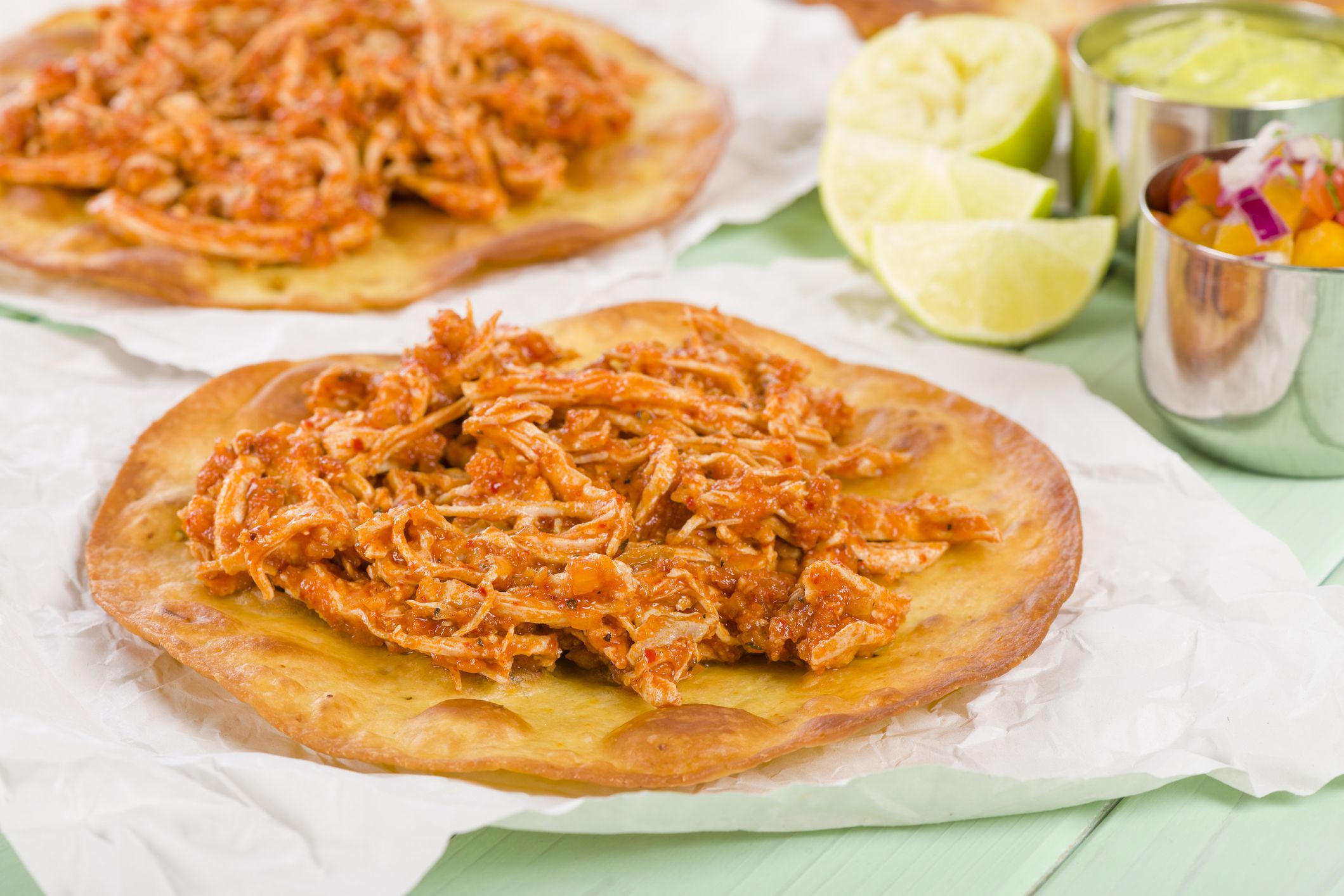 Two instant pot 5-ingredient chicken tacos on serving napkins on a seafoam wooden table with ingredients in the background